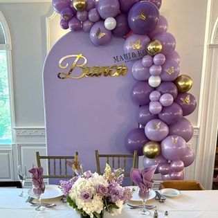 A table with plates , glasses , napkins and flowers in front of a wall covered in purple balloons.