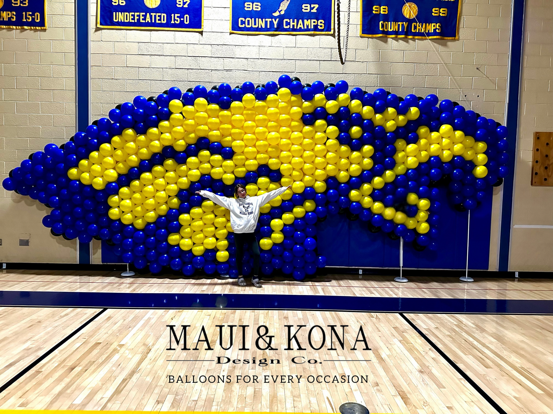 A person standing in front of a wall made of blue and yellow balloons