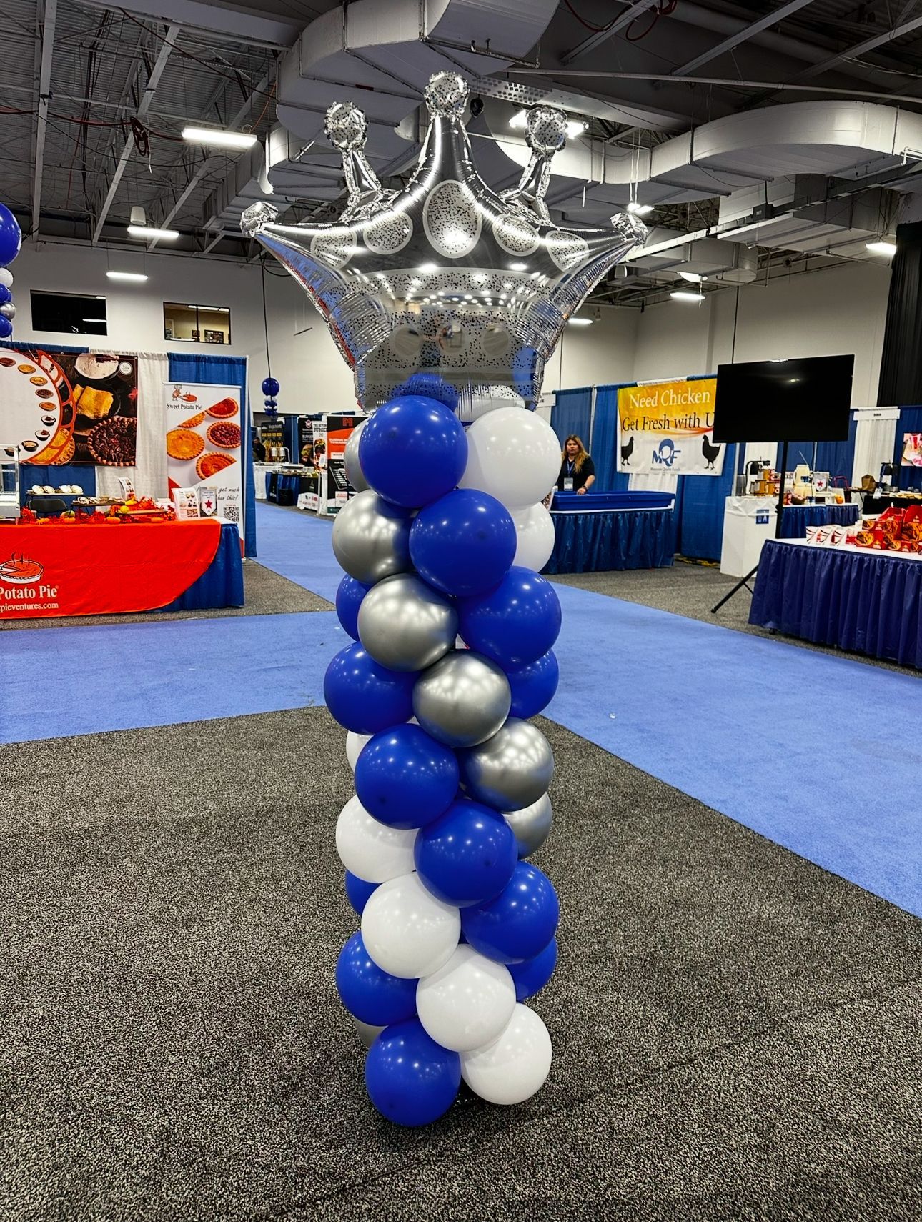 A tower of blue , white and silver balloons with a crown on top.