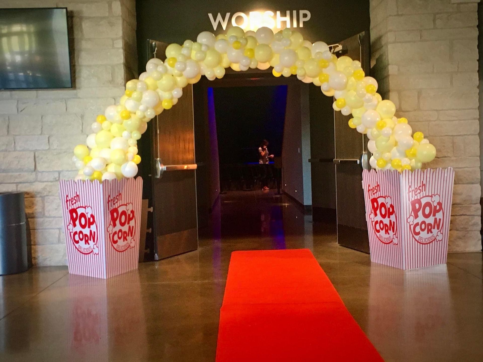 A red carpet is leading to a doorway decorated with balloons and popcorn boxes.