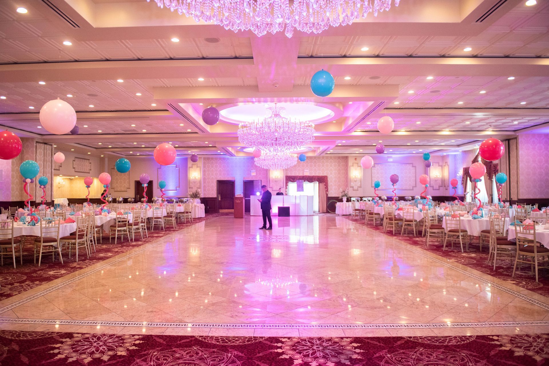 A large ballroom filled with tables and chairs and balloons.