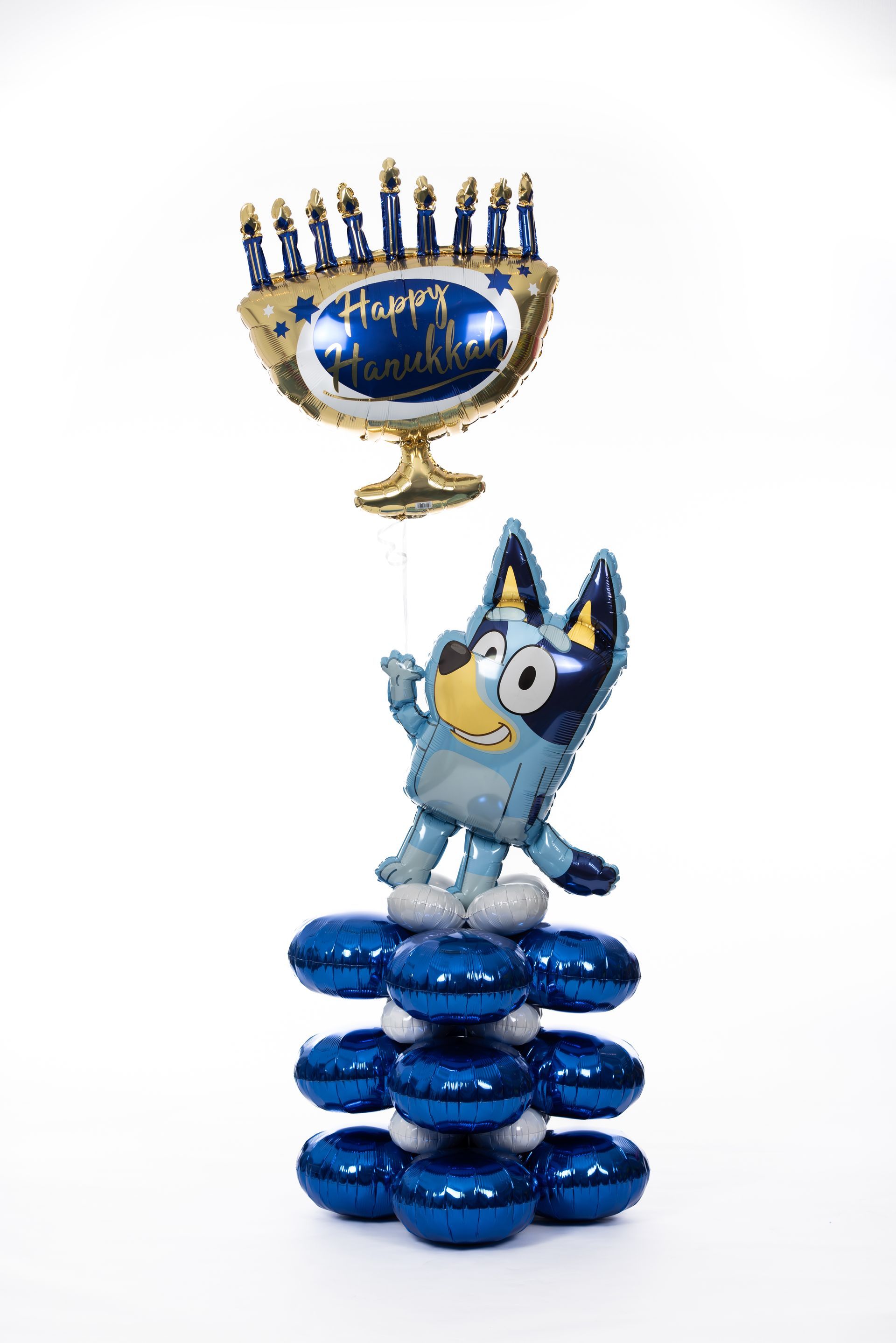A blue dog is standing on top of a stack of blue balloons next to a menorah.