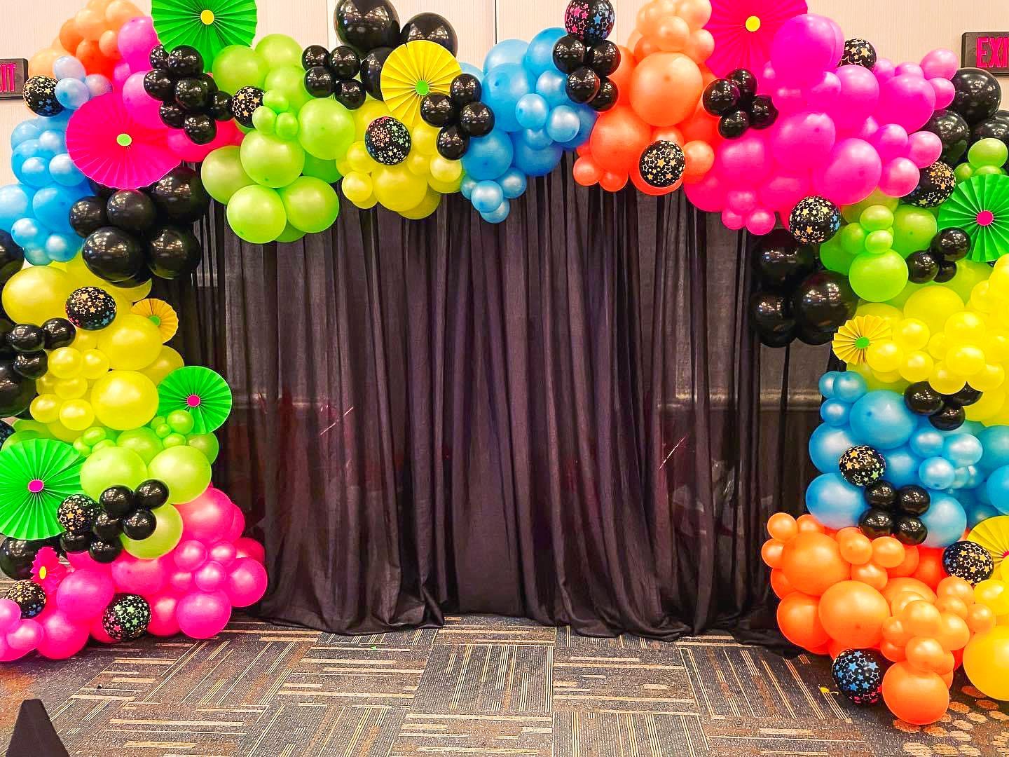 A bunch of colorful balloons are sitting in front of a black curtain.
