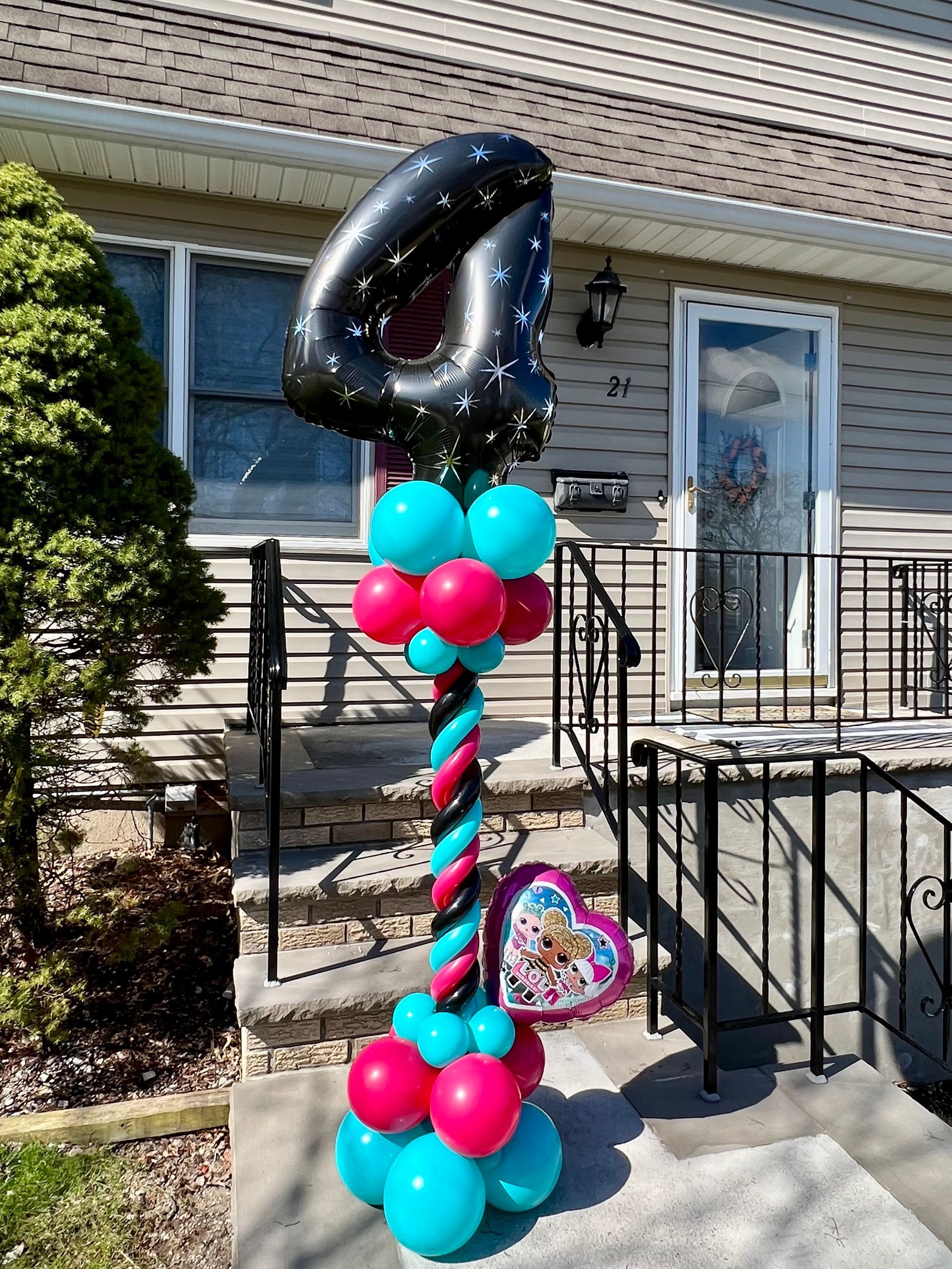 A balloon tower with a number four balloon on top of it in front of a house.