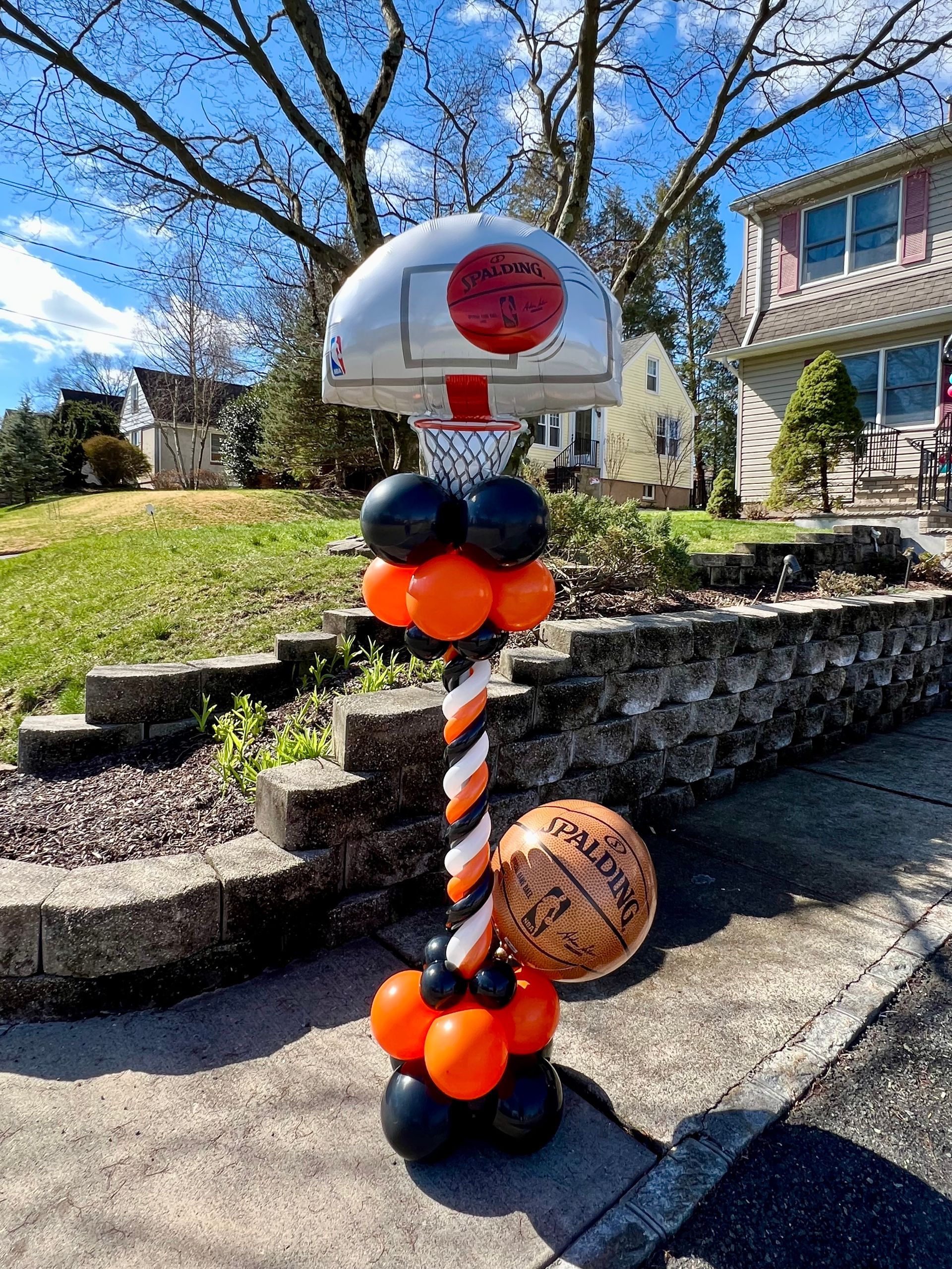 A basketball hoop is decorated with balloons in front of a house.