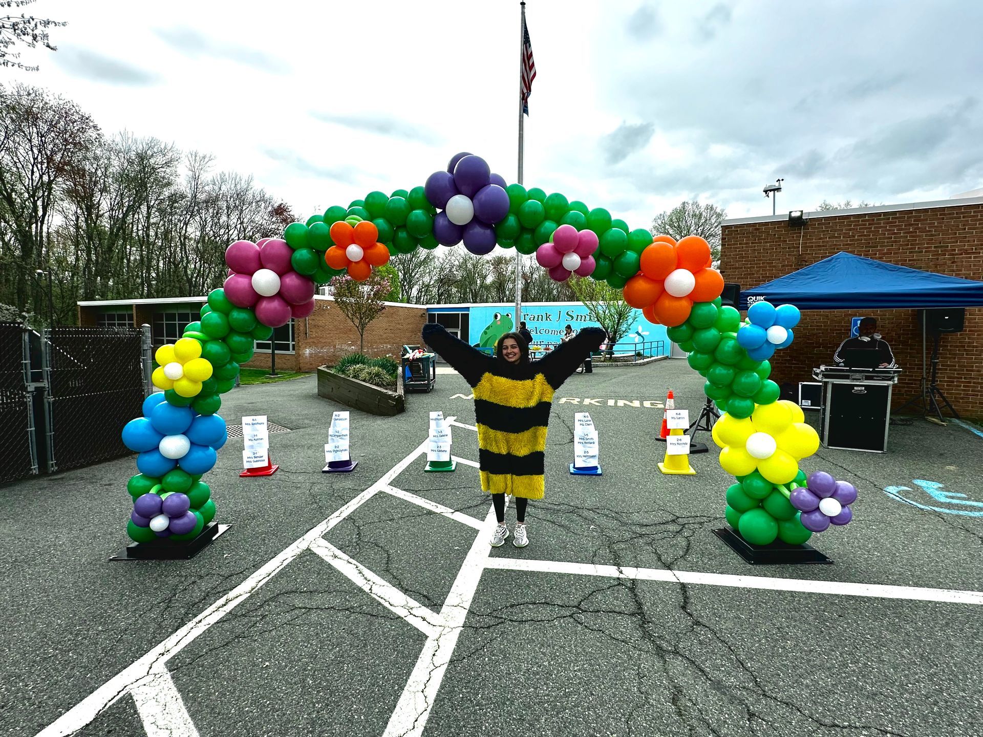 A woman in a bee costume is standing under a balloon arch.