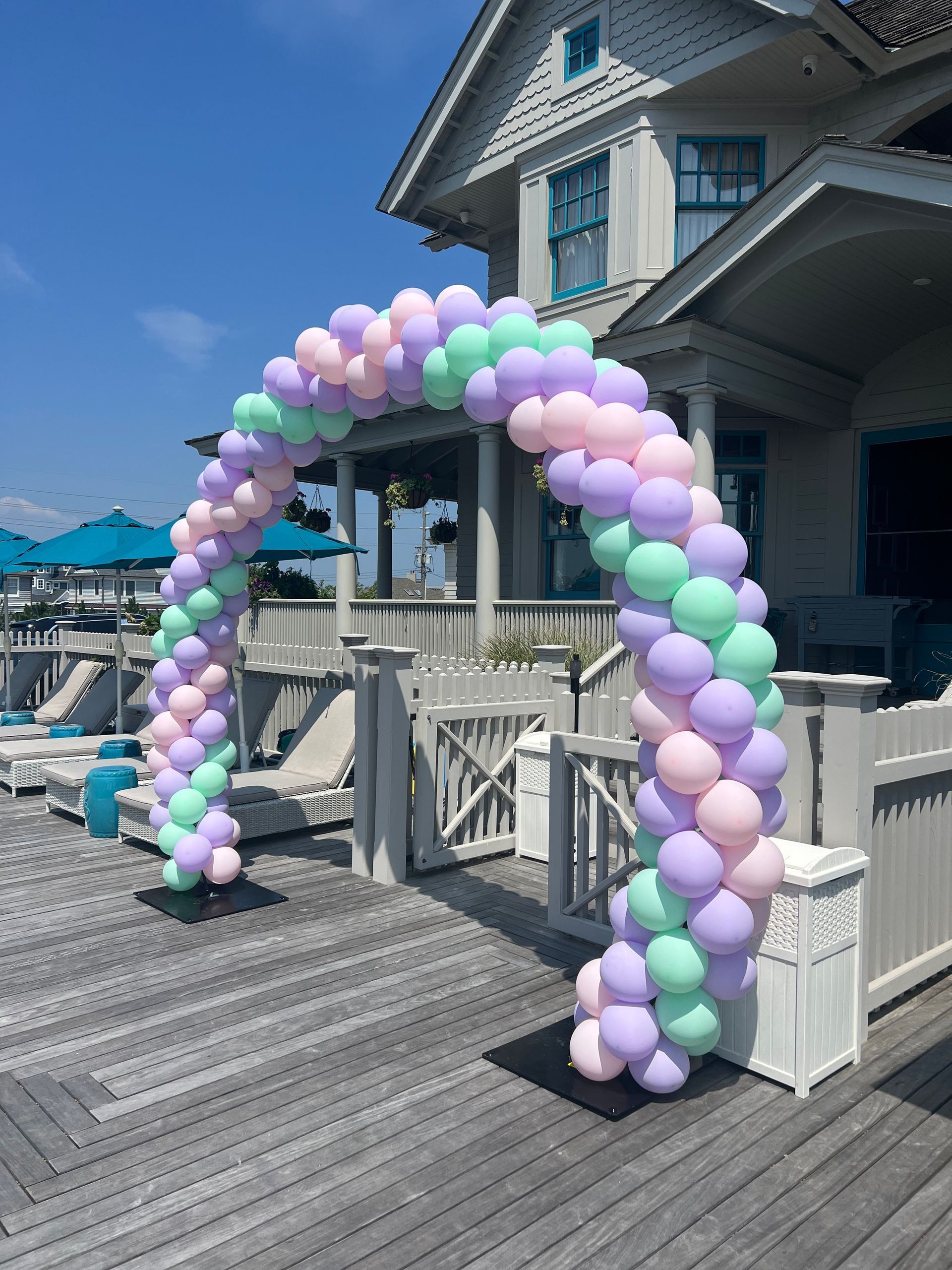 A balloon arch is sitting on a wooden deck in front of a house.