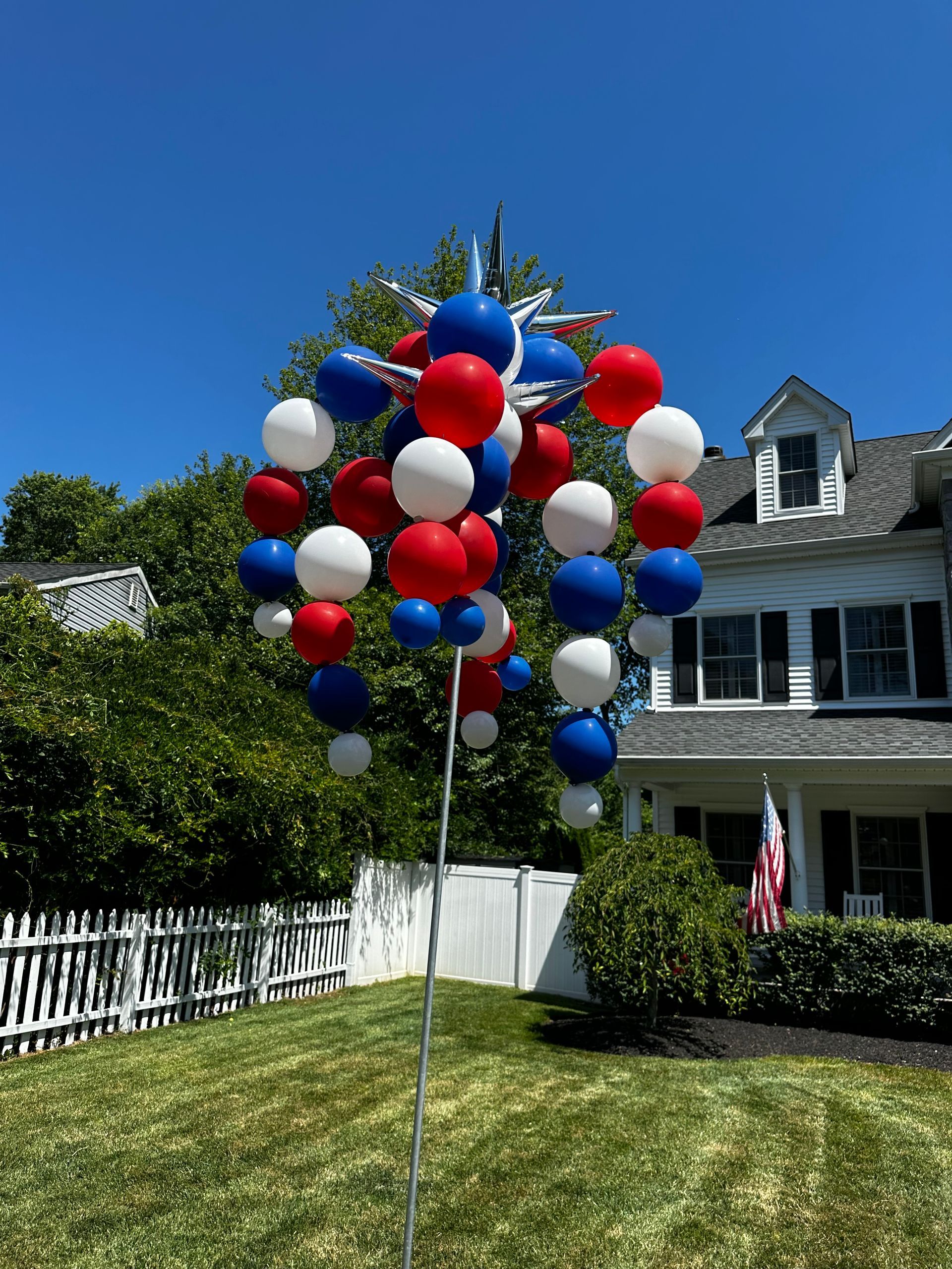 A bunch of red , white and blue balloons on a pole in front of a house.