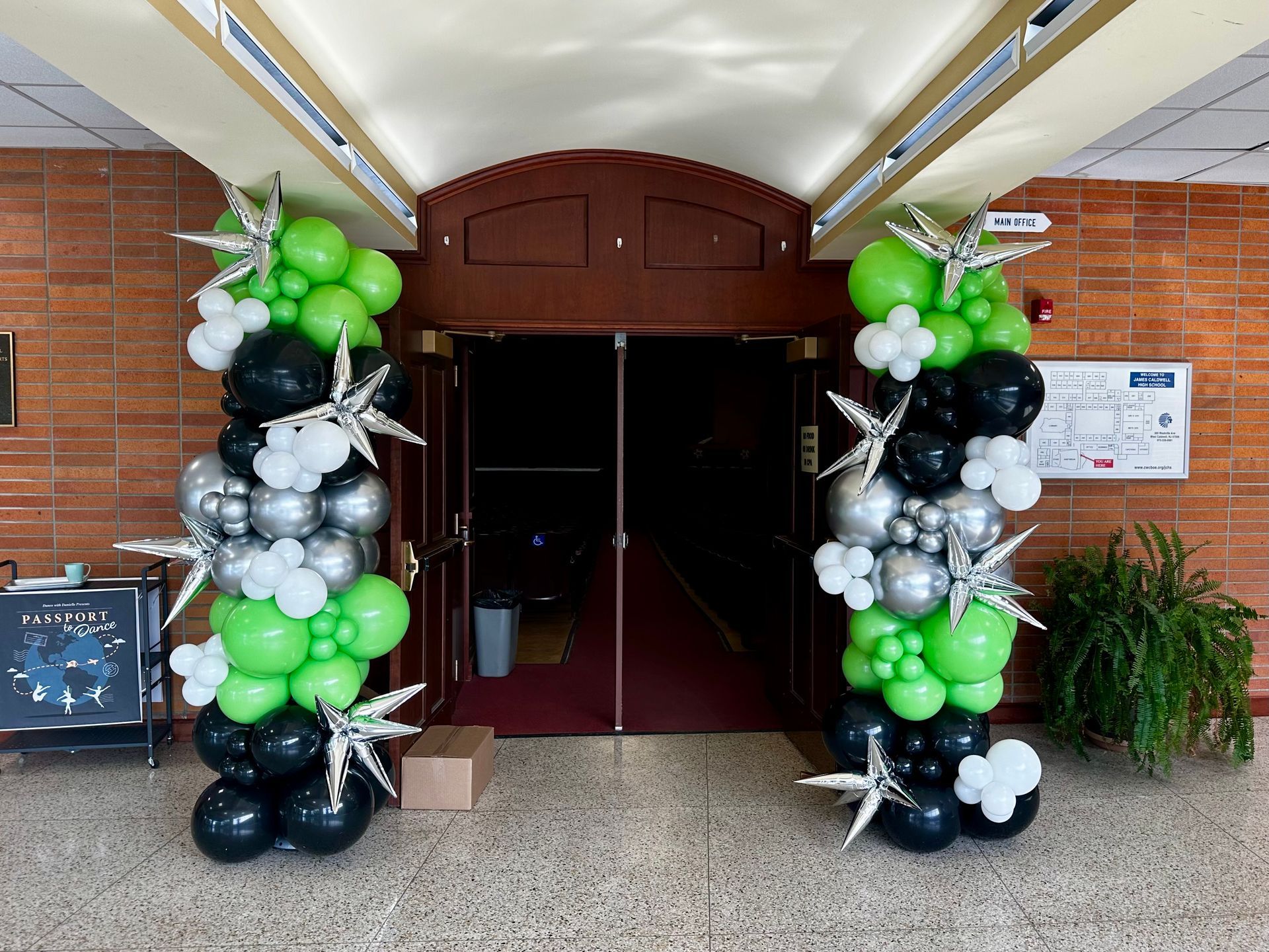 A row of green , black , and silver balloons are lined up in front of a doorway.
