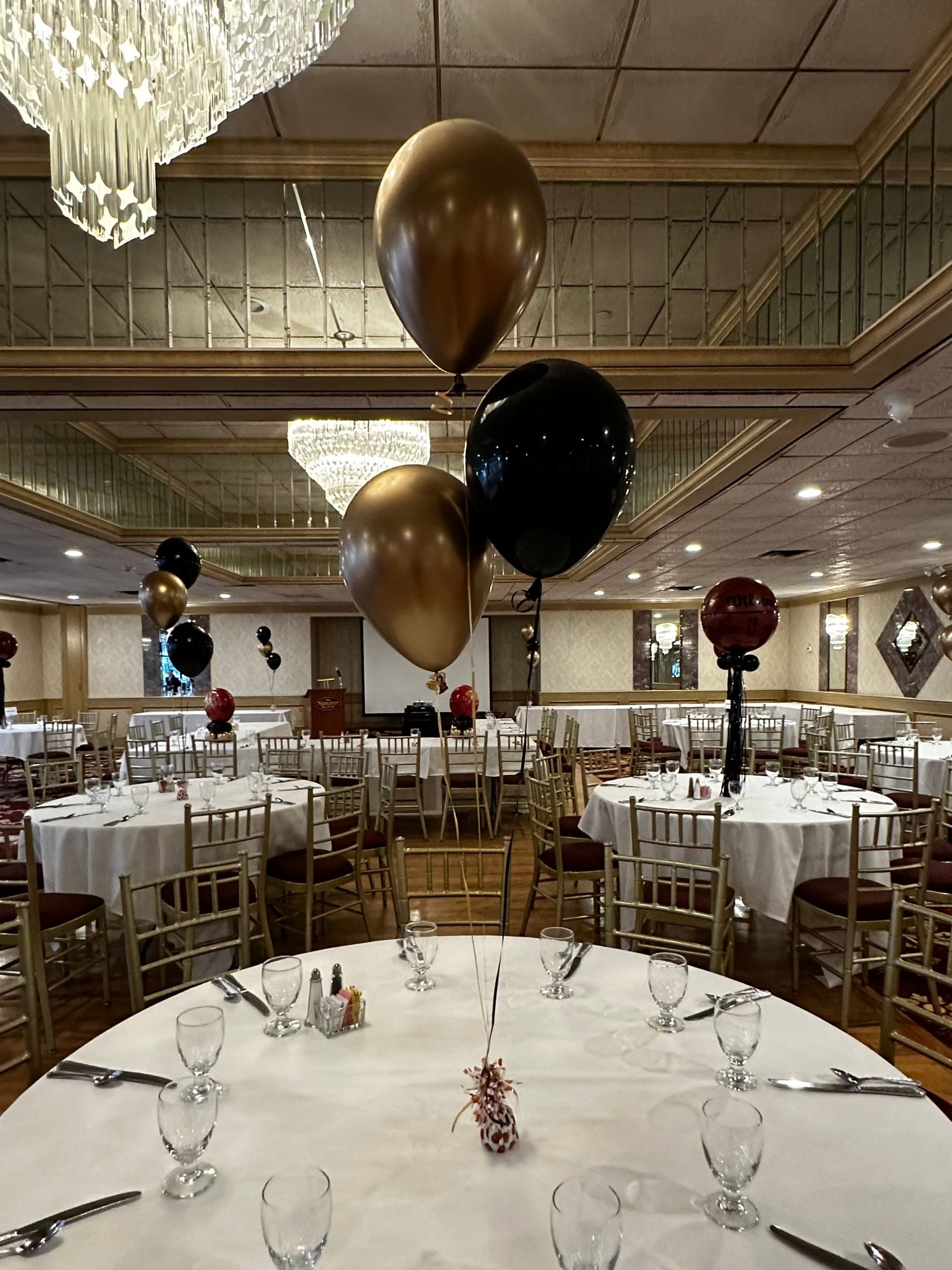 A large room with tables and chairs and balloons hanging from the ceiling.