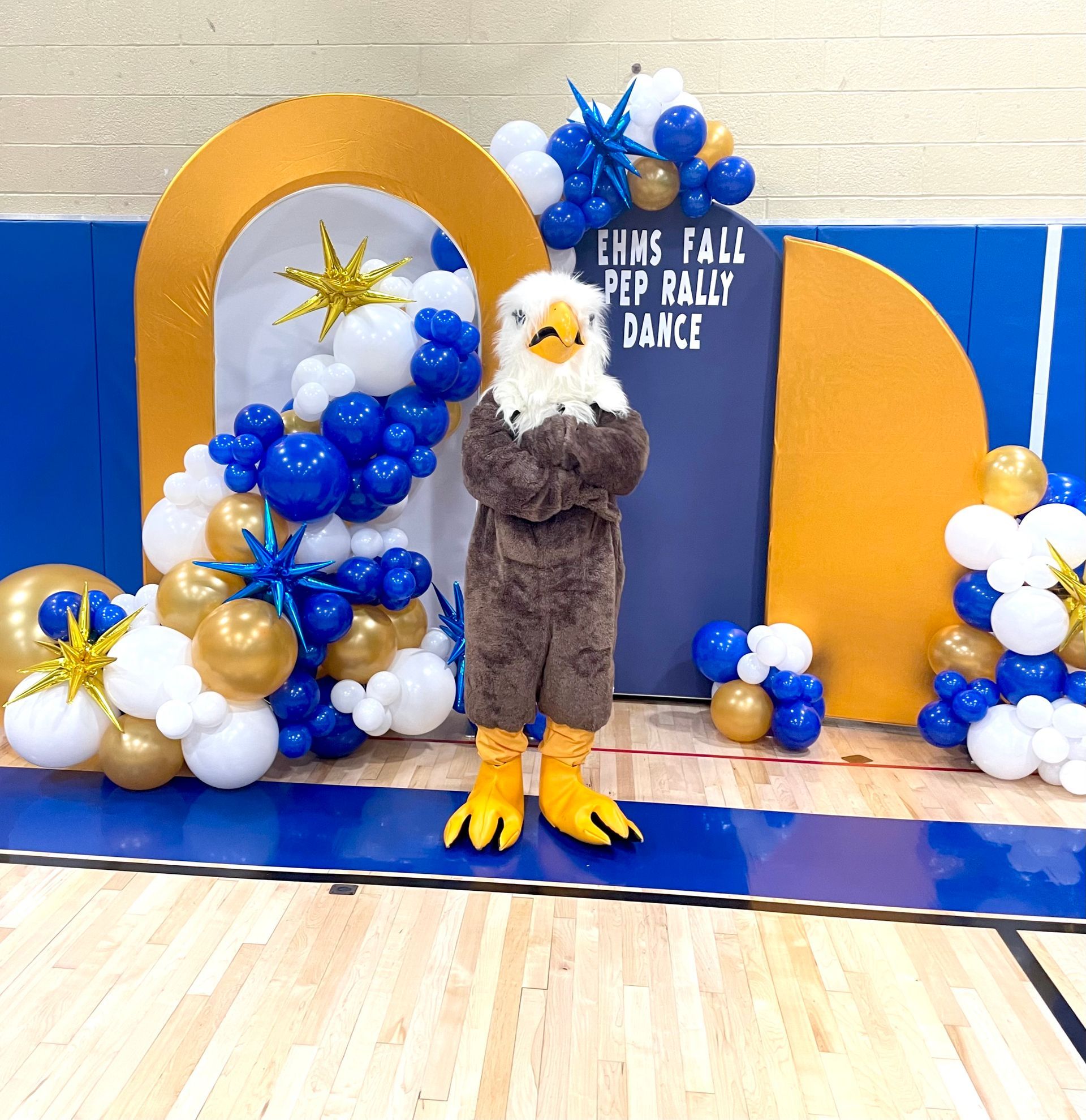 A mascot in front of a sign that says ' ehms fall pep rally dance '