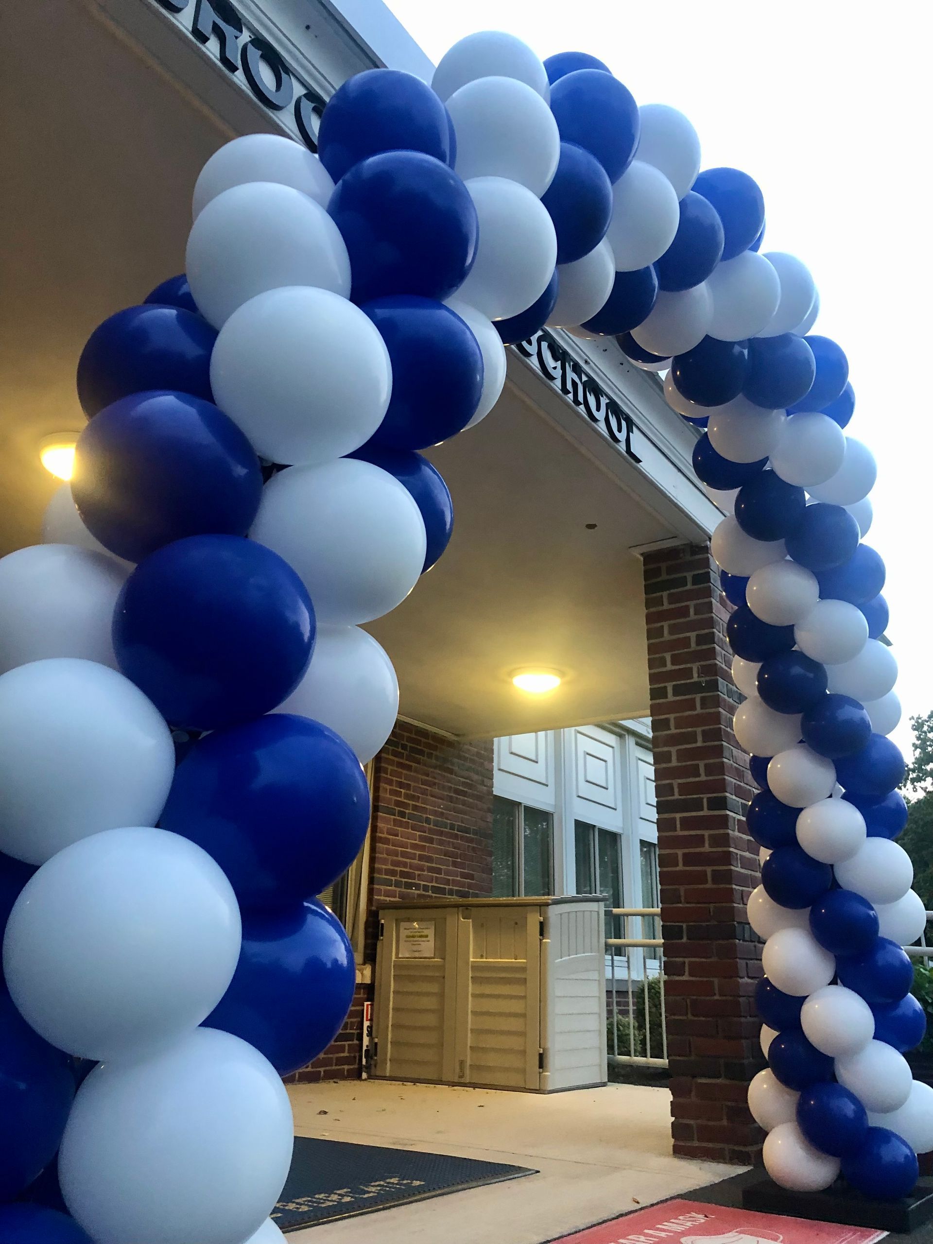A blue and white balloon arch is in front of a brick building.