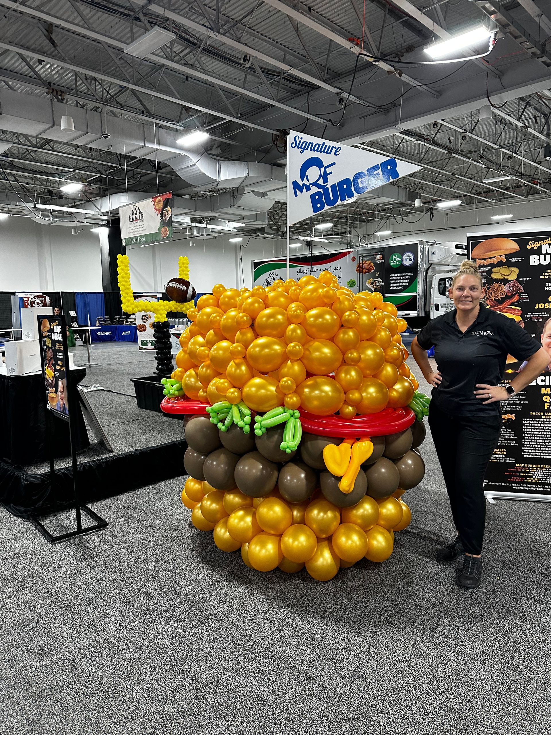 A woman is standing next to a giant hamburger made out of balloons.