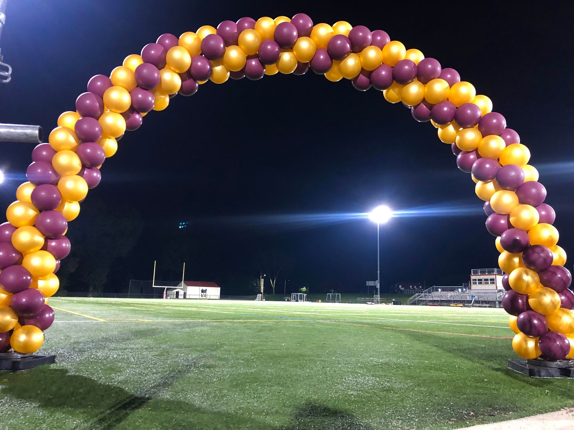 A large arch made of yellow and maroon balloons on a football field.