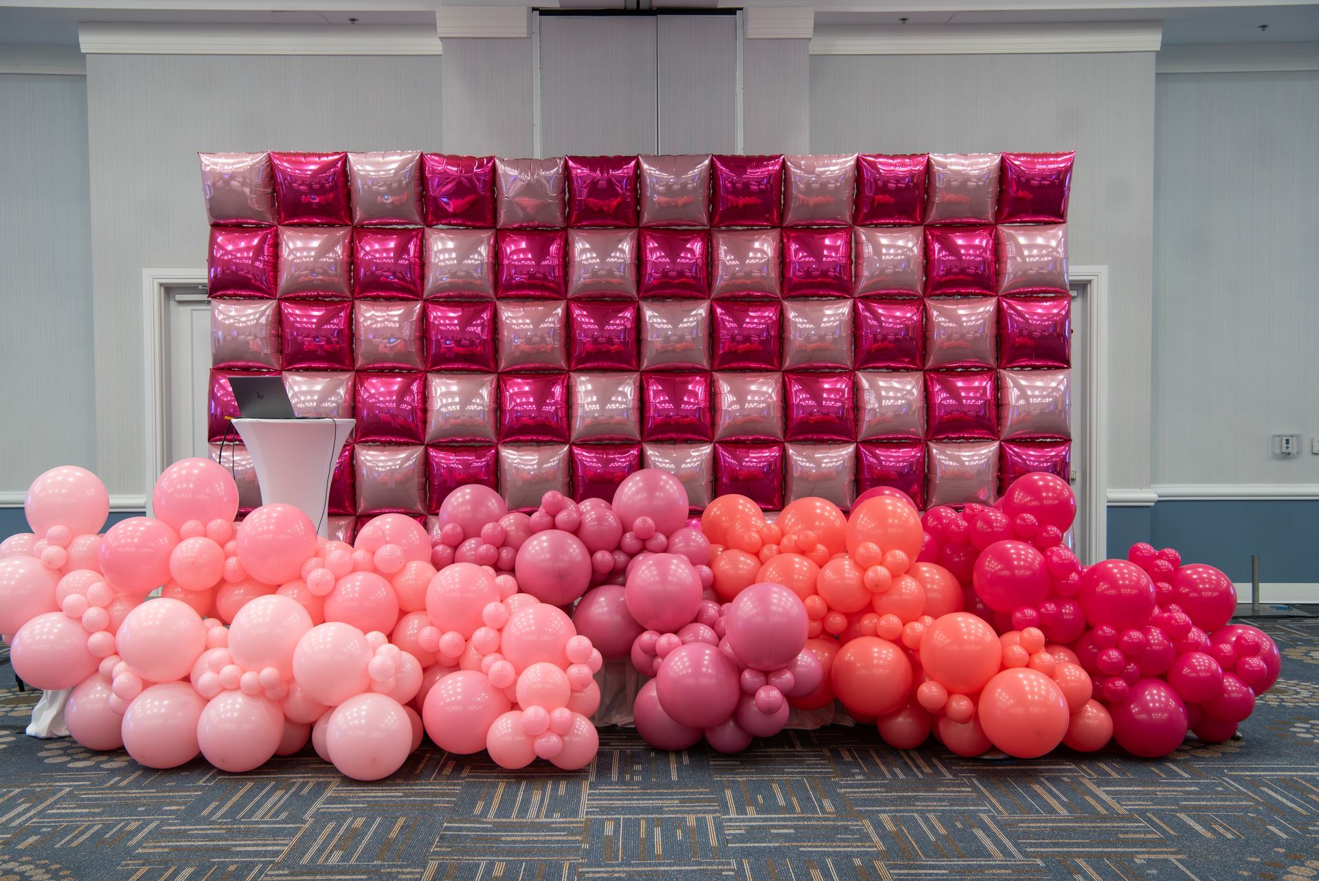 A wall of pink and orange balloons in a room.