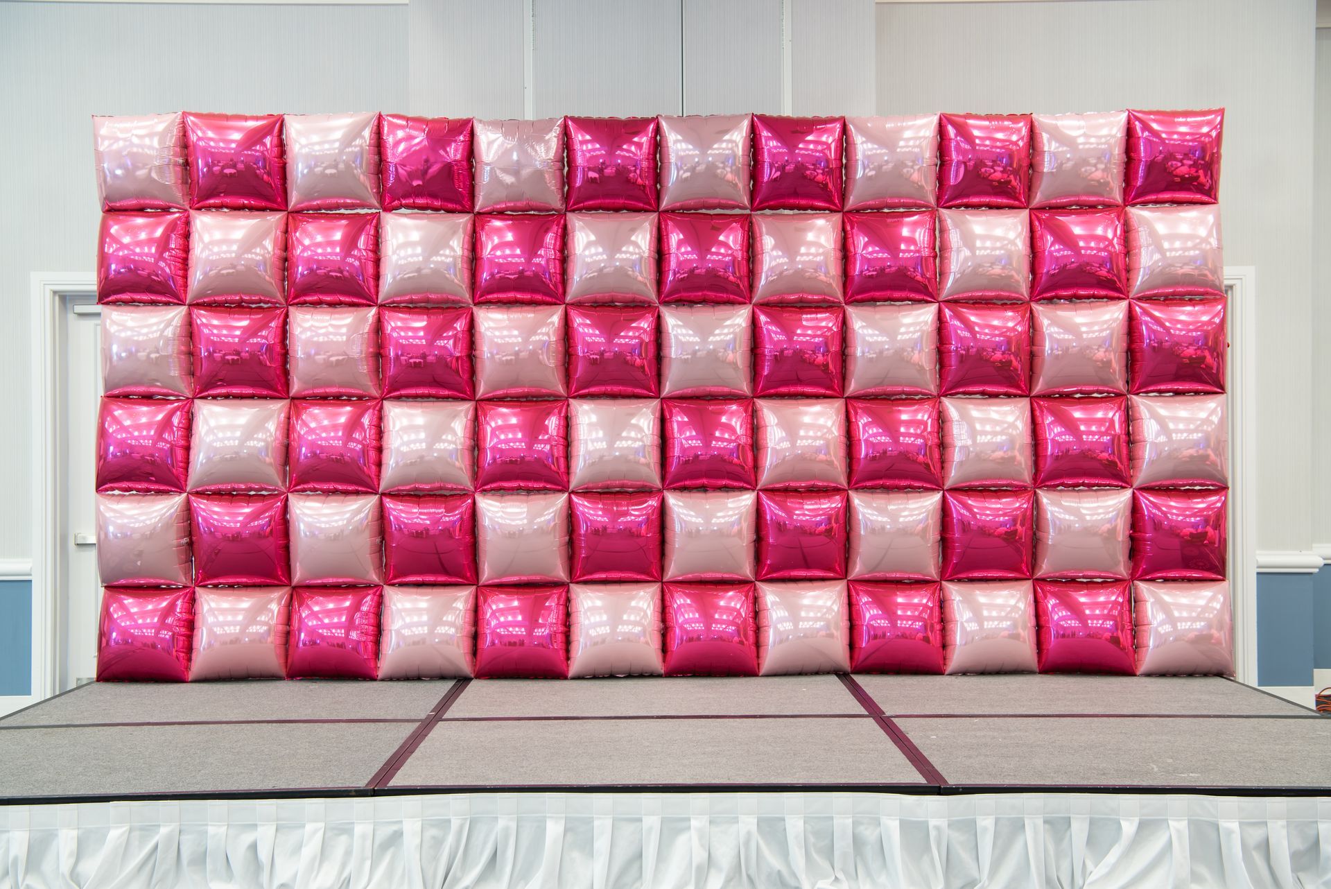 A wall made of pink and white balloons on a stage.