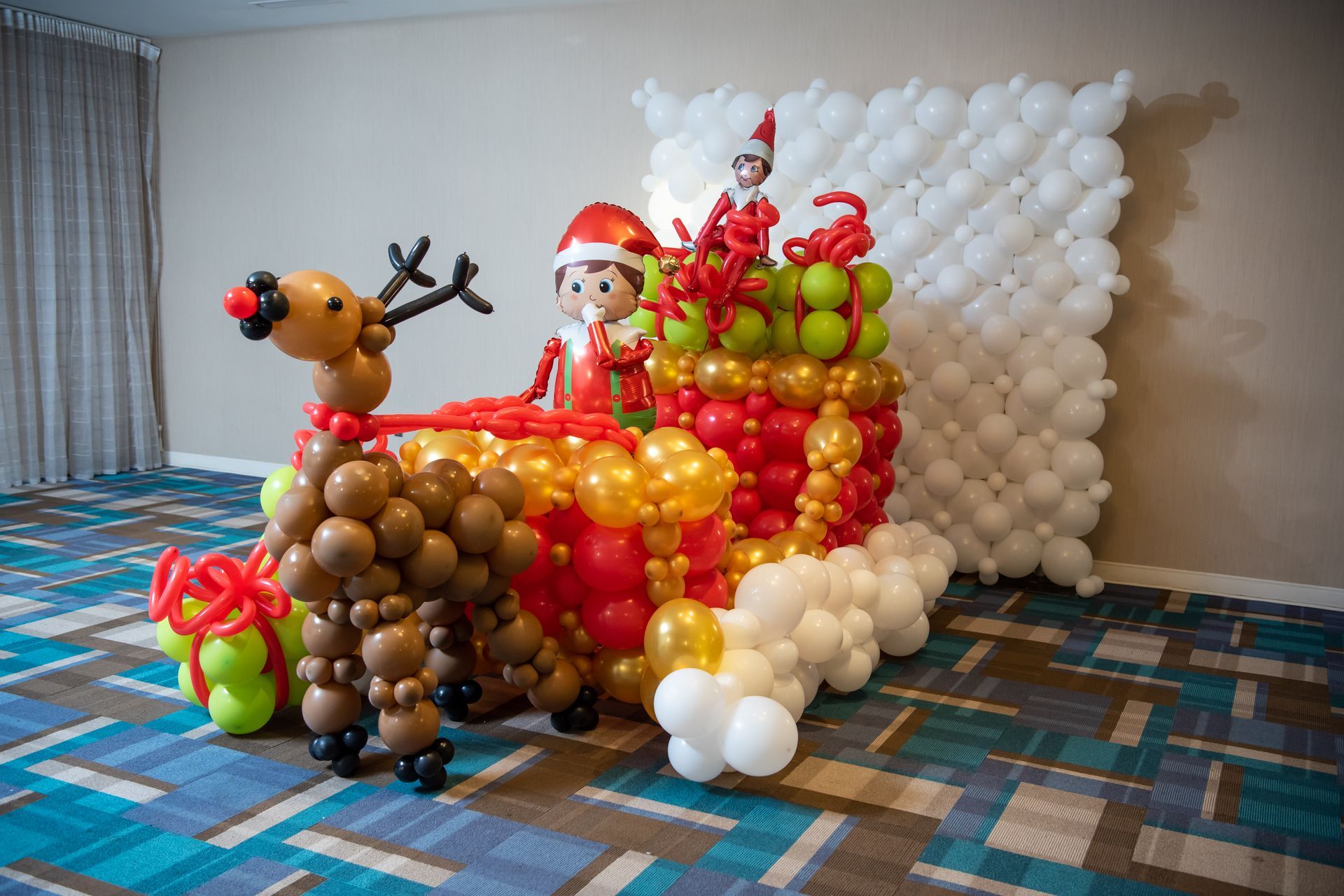 An elf on the shelf is pulling a sleigh made of balloons.