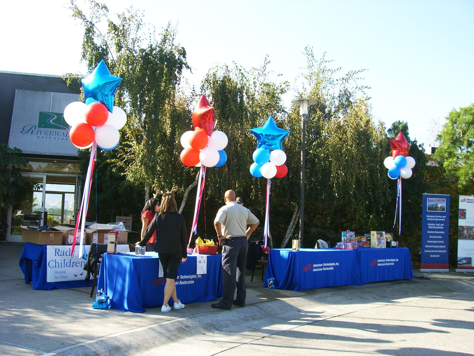 People standing in front of tables with red white and blue balloons