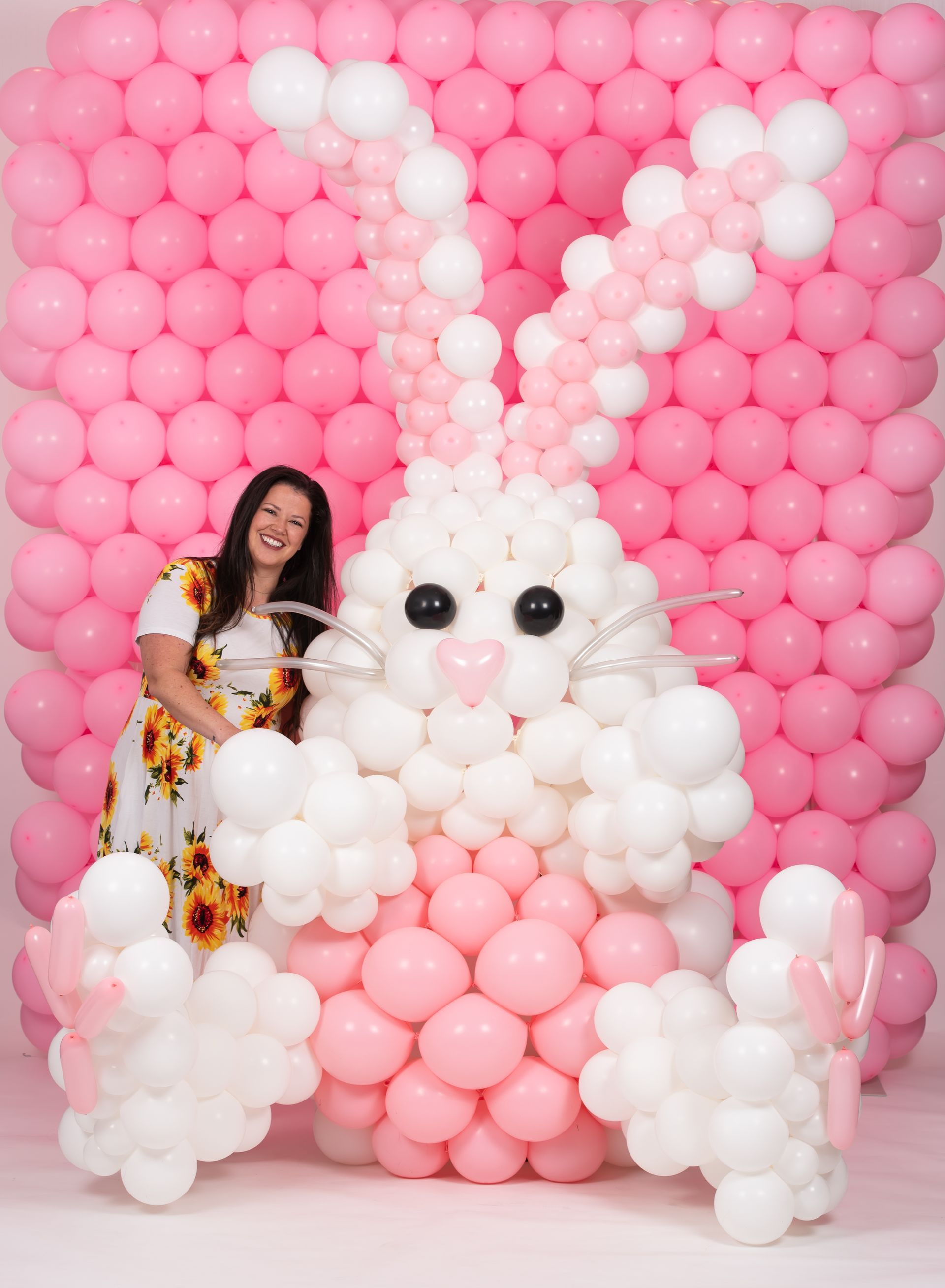 A woman is standing in front of a bunny made out of balloons.