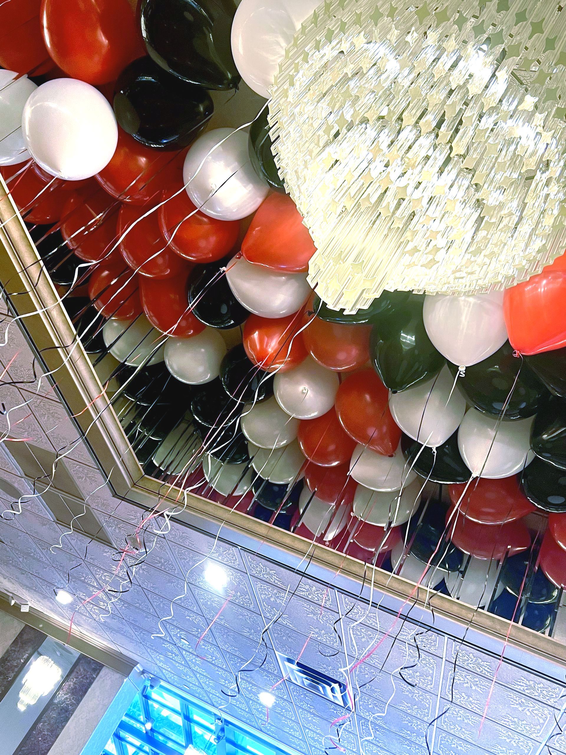 Ceiling decorated with red, white, black balloons and a large chandelier.