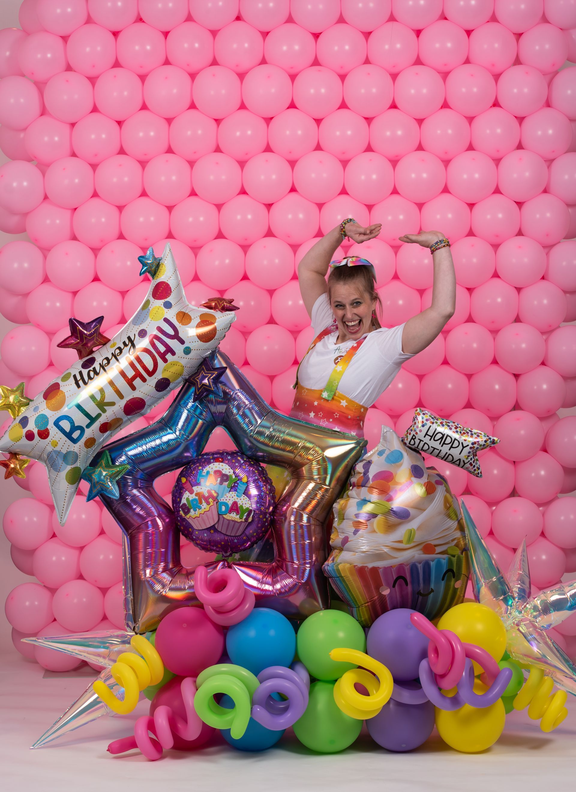A woman is standing in front of a wall of pink balloons.