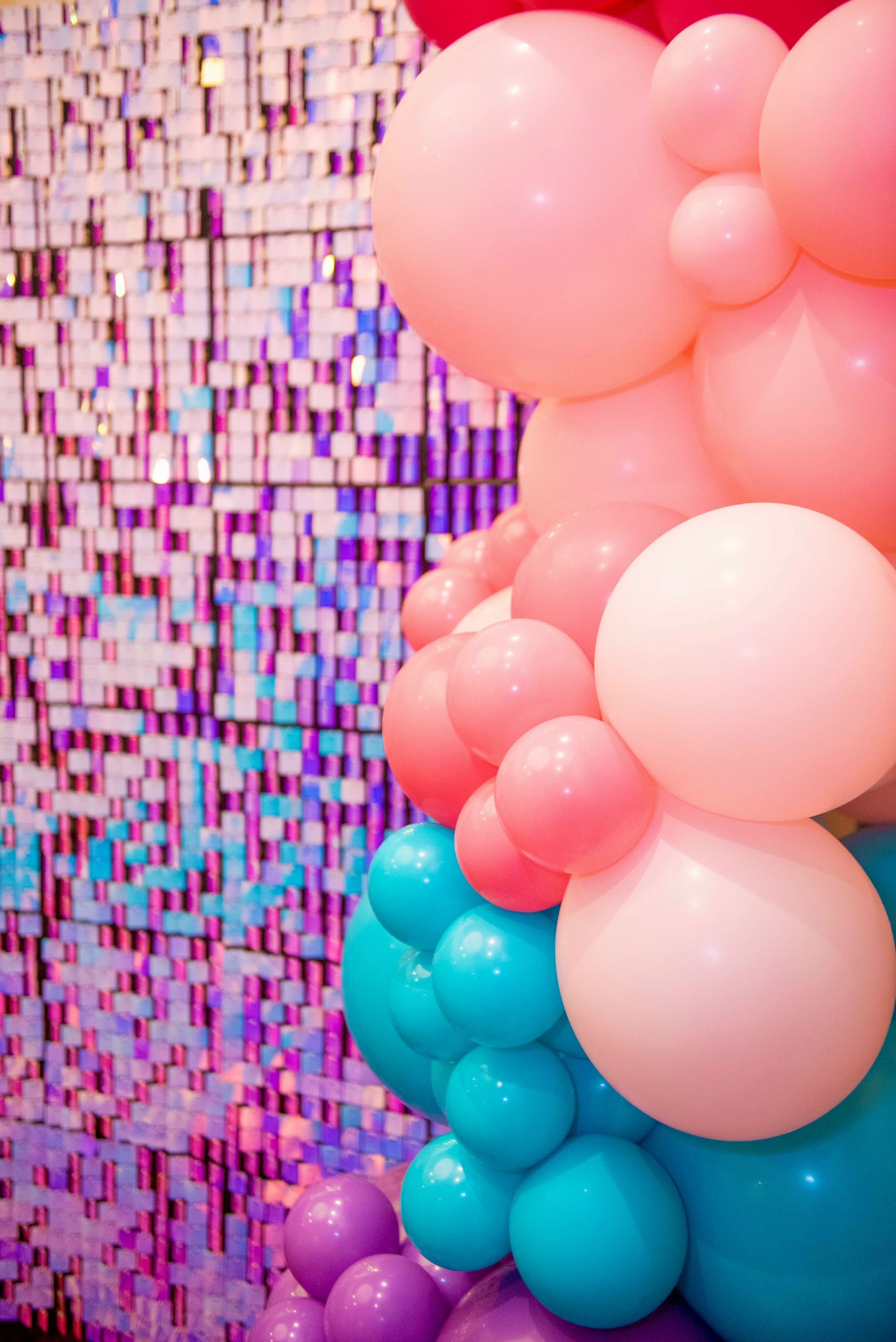 A bunch of pink , blue , and purple balloons are hanging from a wall.