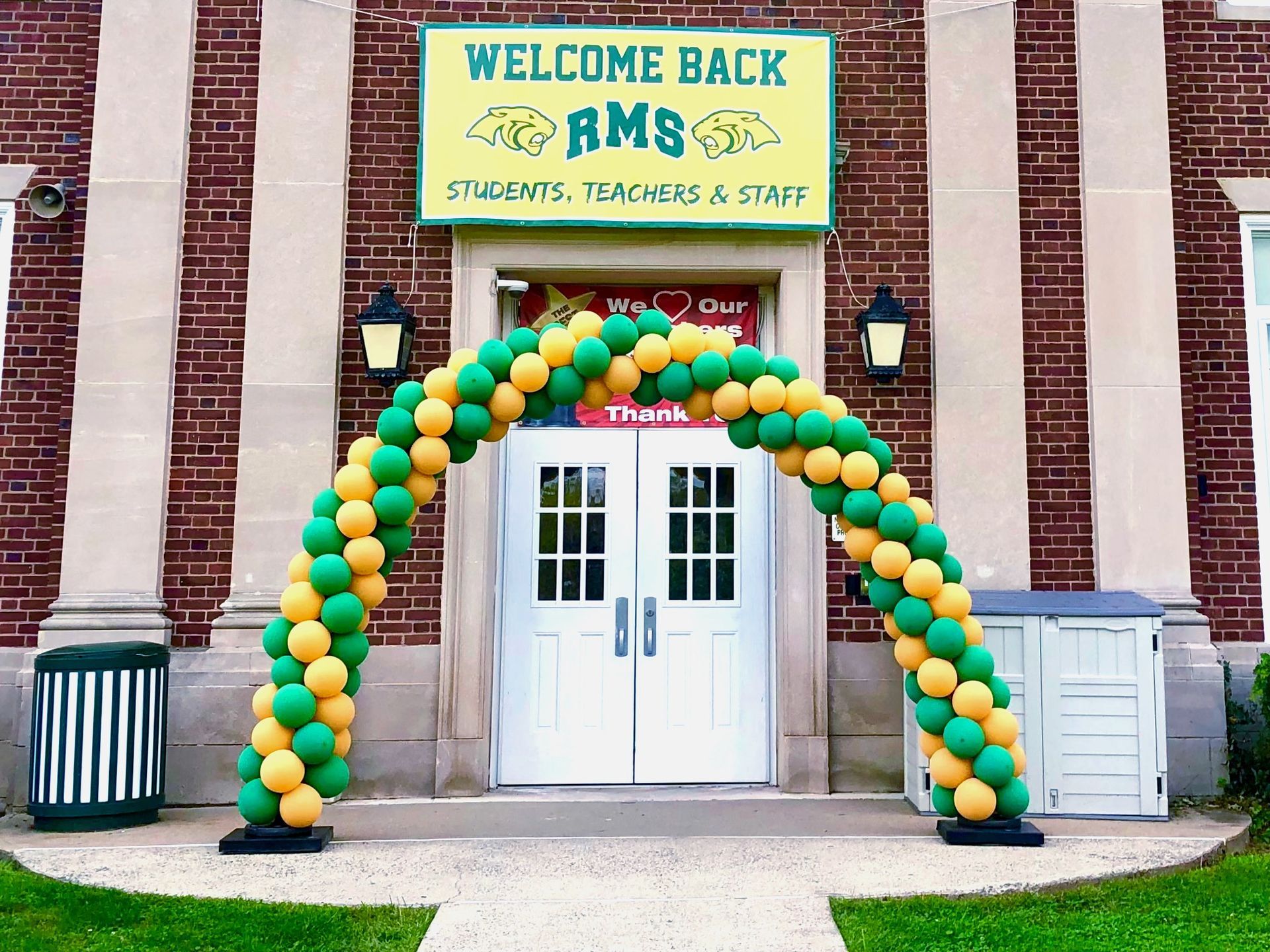 A green and yellow balloon arch in front of a building that says welcome back rams