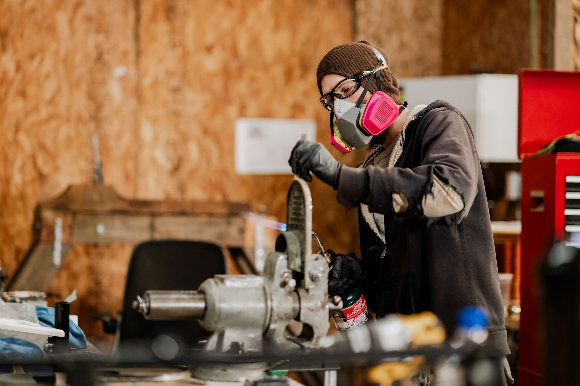 Person in a workshop wearing a respirator, working on machinery with gloves, workbench setting | Photos by Kodjoarts