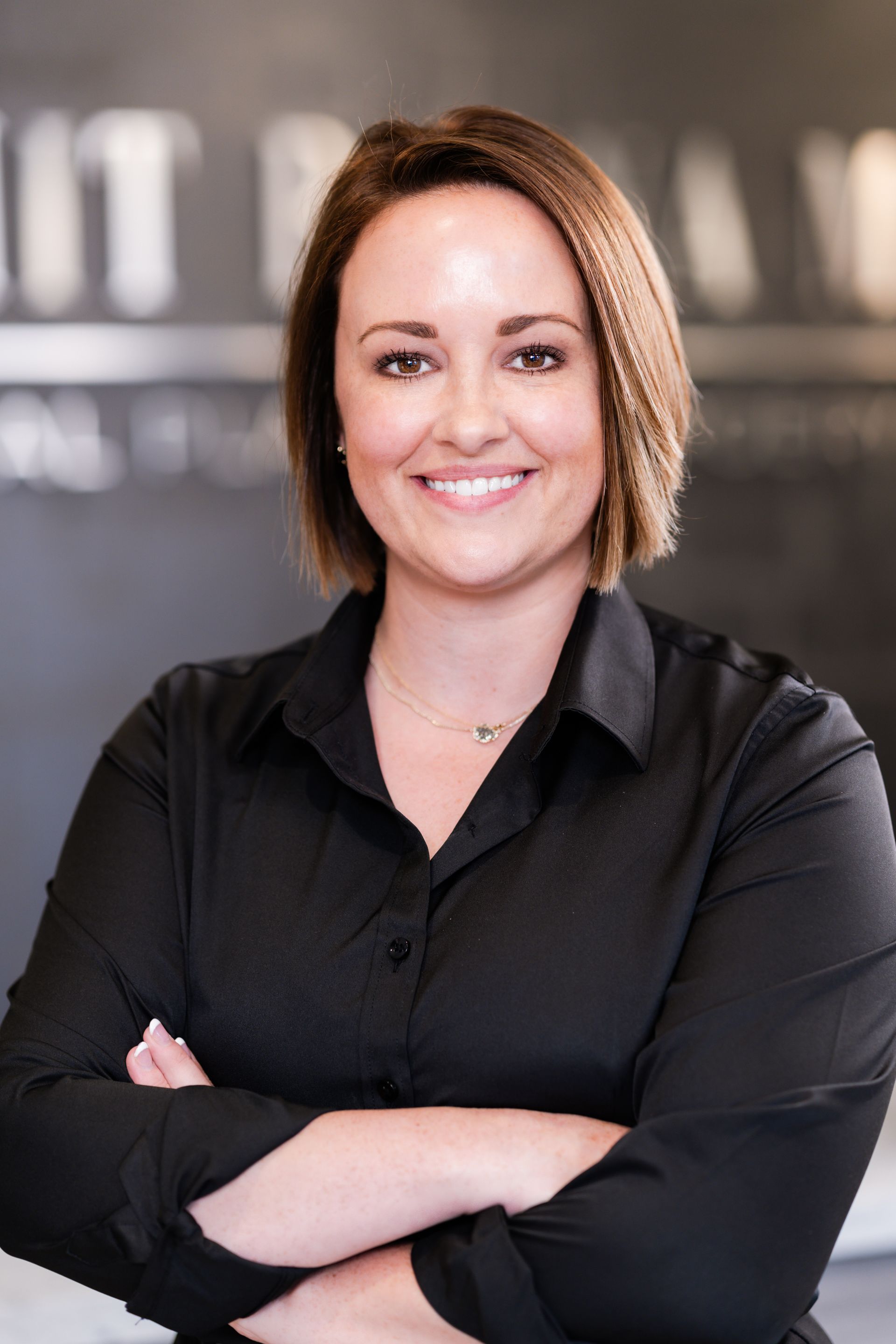 A woman in a black shirt is standing with her arms crossed and smiling.