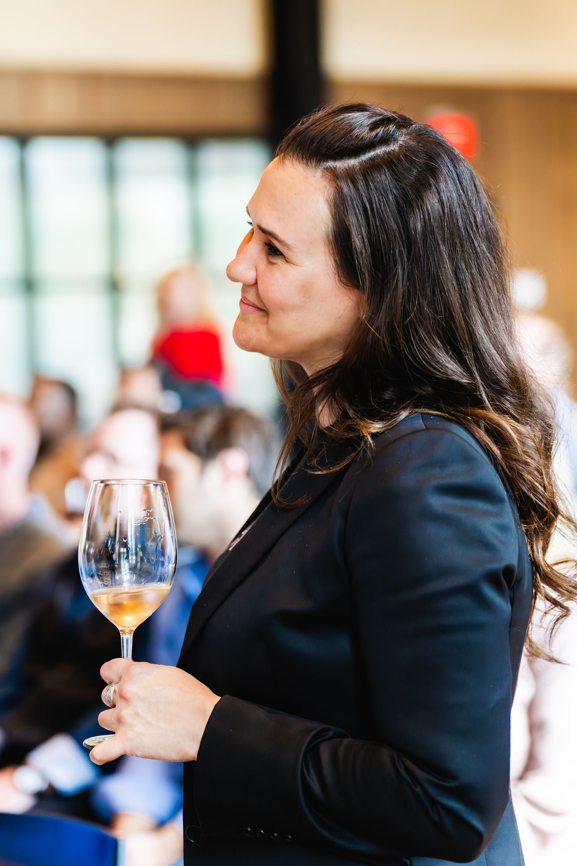A woman in a black suit is holding a glass of wine.