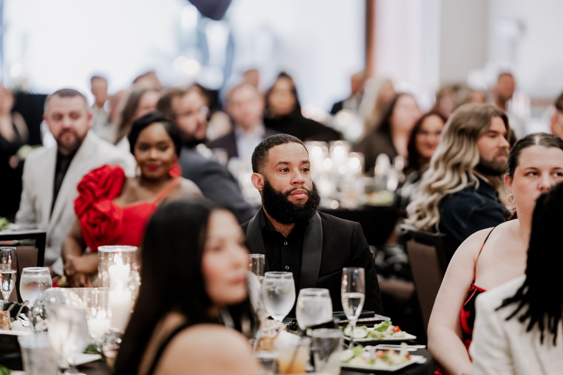 Guests sit at tables in a dimly lit banquet hall, focused on an event during a formal dinner gathering.