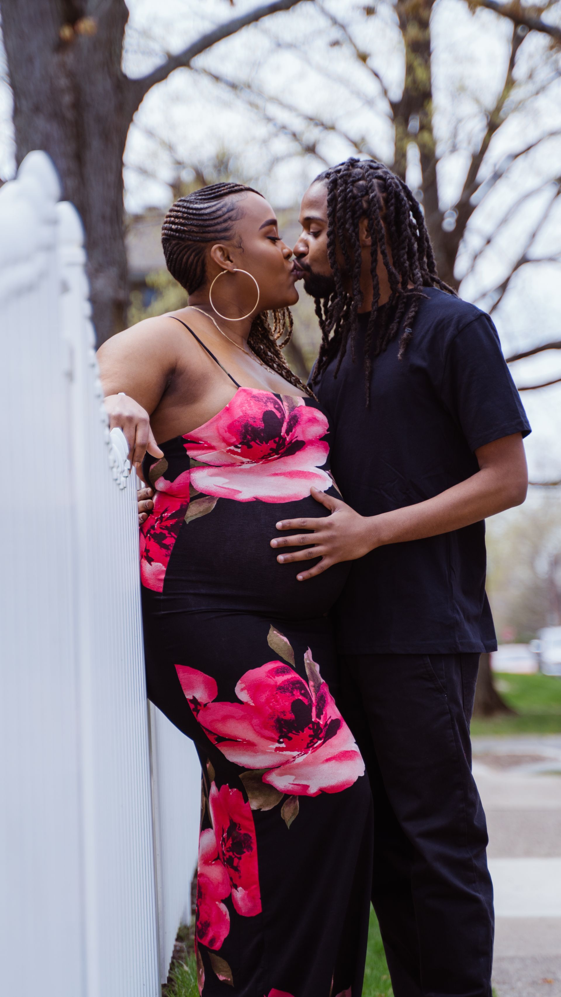 a man is kissing a pregnant woman on the cheek while standing next to a white fence .