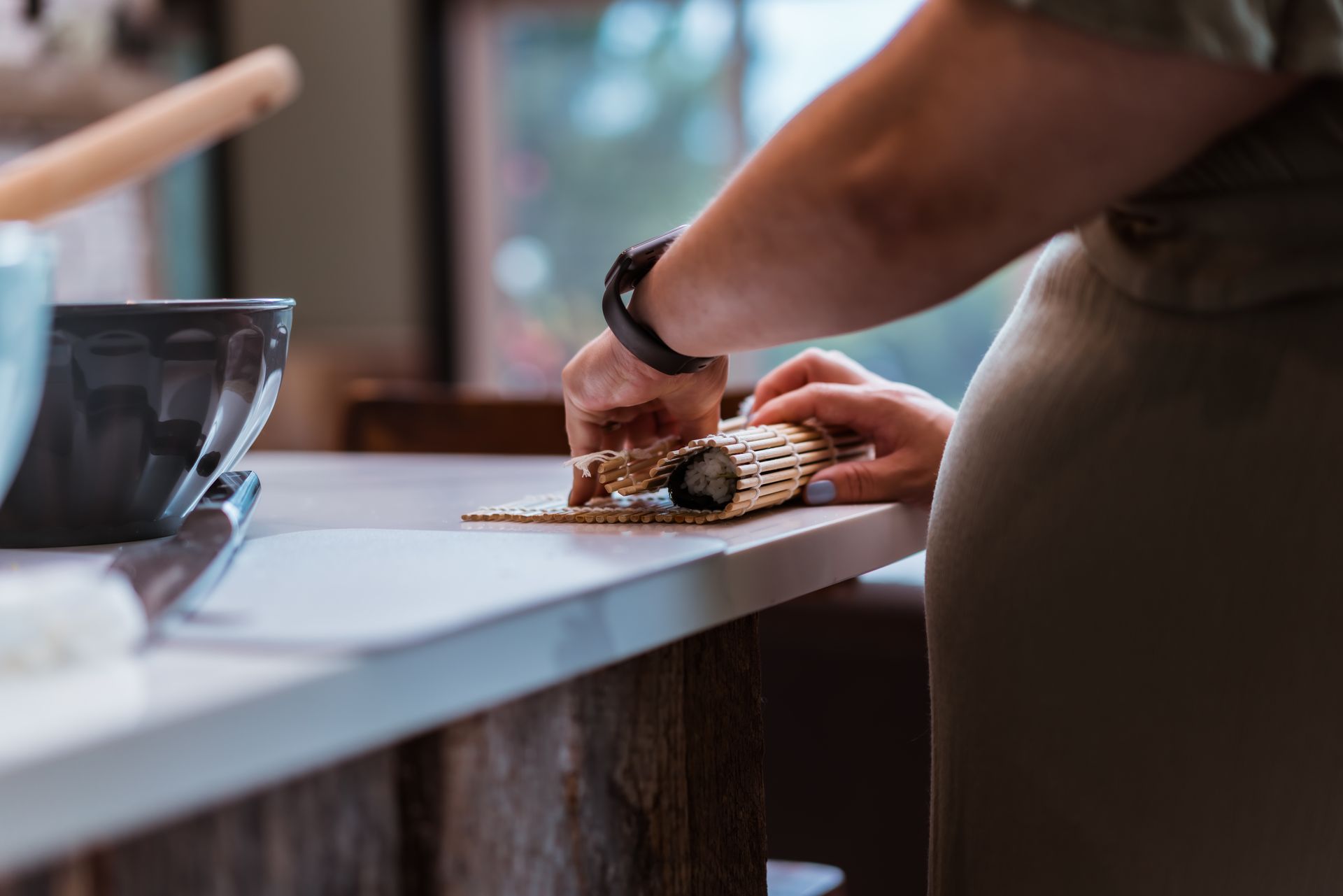 Person rolling sushi on a countertop, using a bamboo mat.