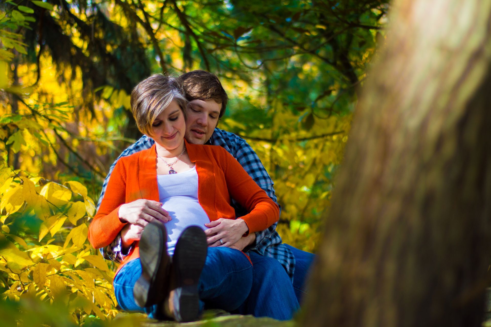 a man and a pregnant woman are sitting next to each other in the woods .