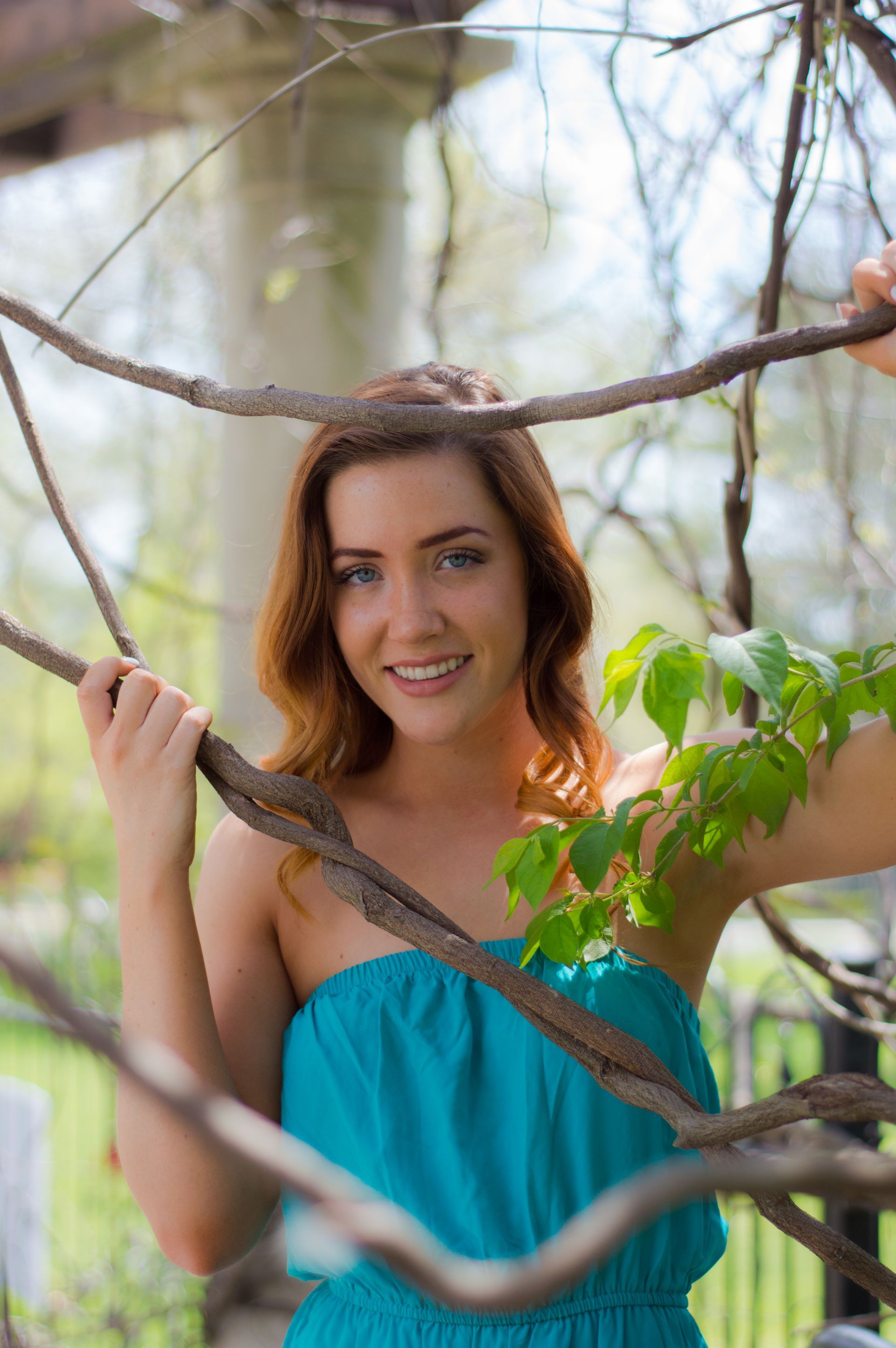 a woman in a blue dress is standing in a tree holding a branch .