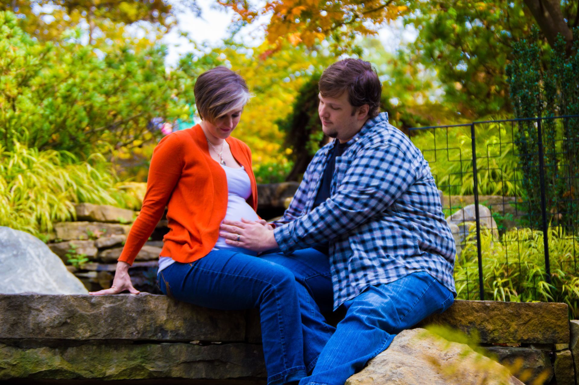 a man and a pregnant woman are sitting on a rock in a park .
