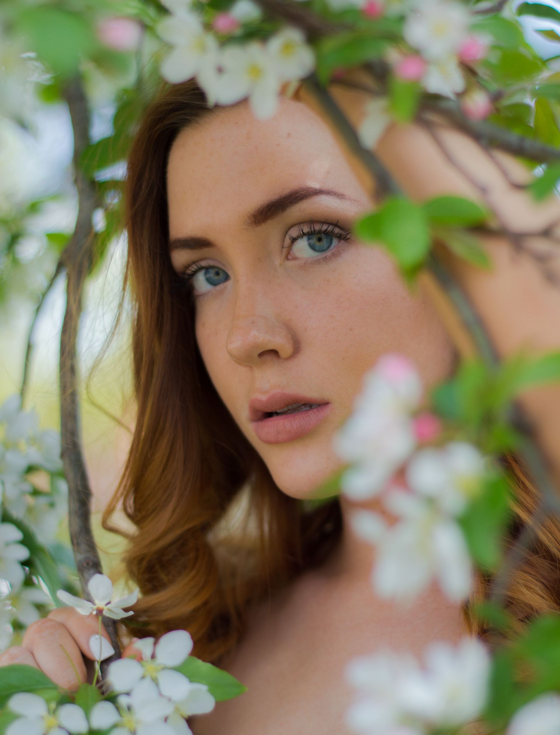 High school senior standing under a tree with white flowers .