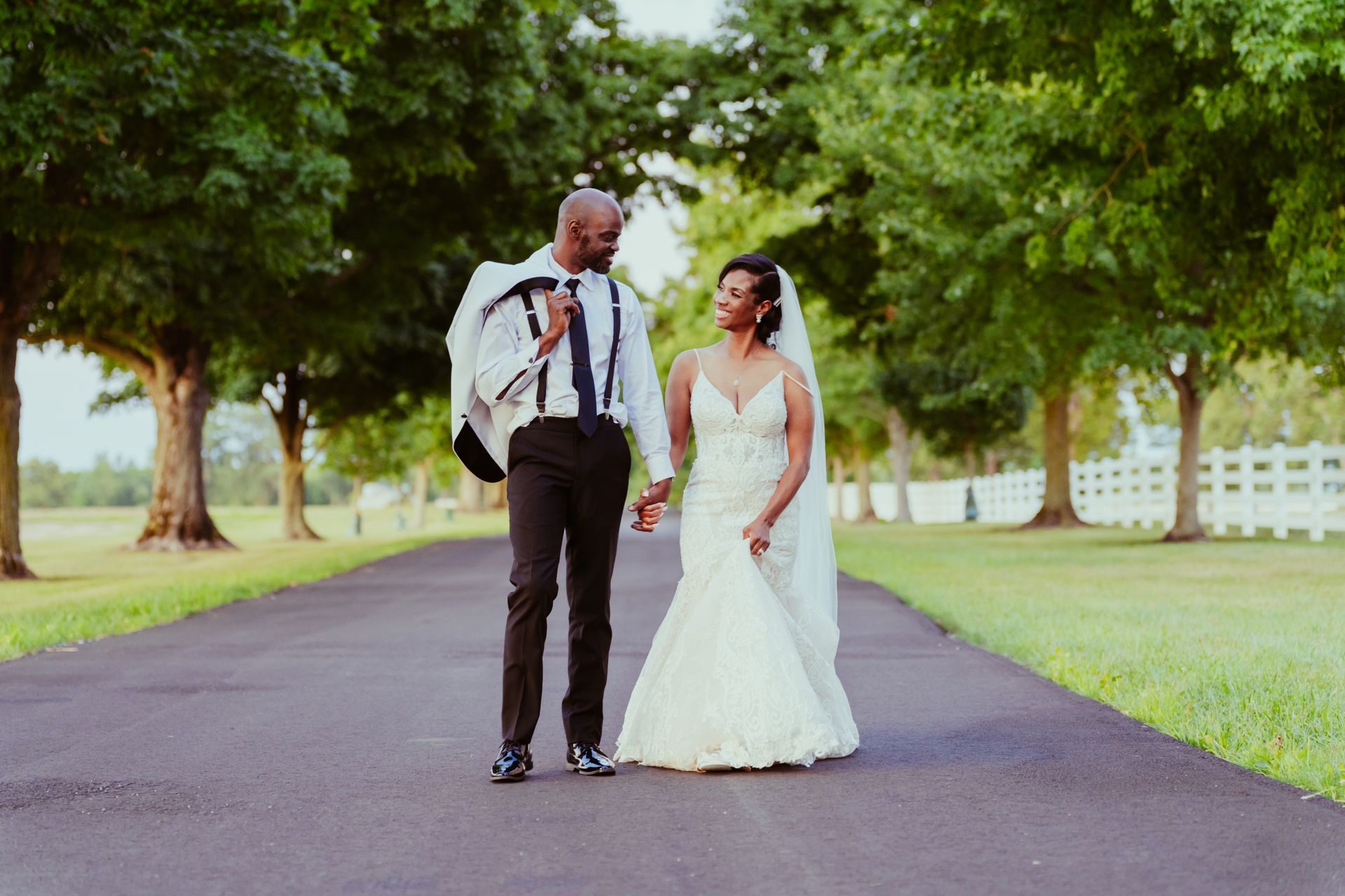A bride and groom are walking down a path holding hands.