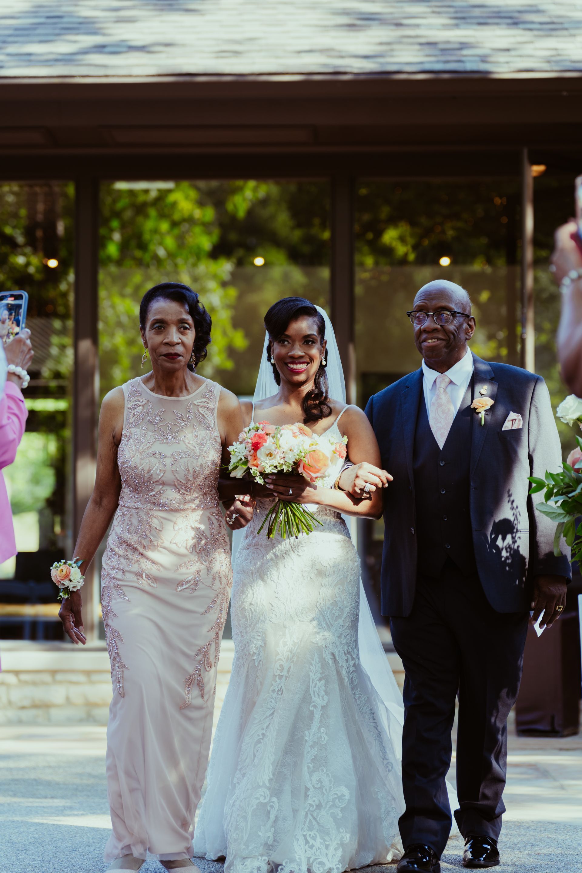 A bride is walking down the aisle with her parents.