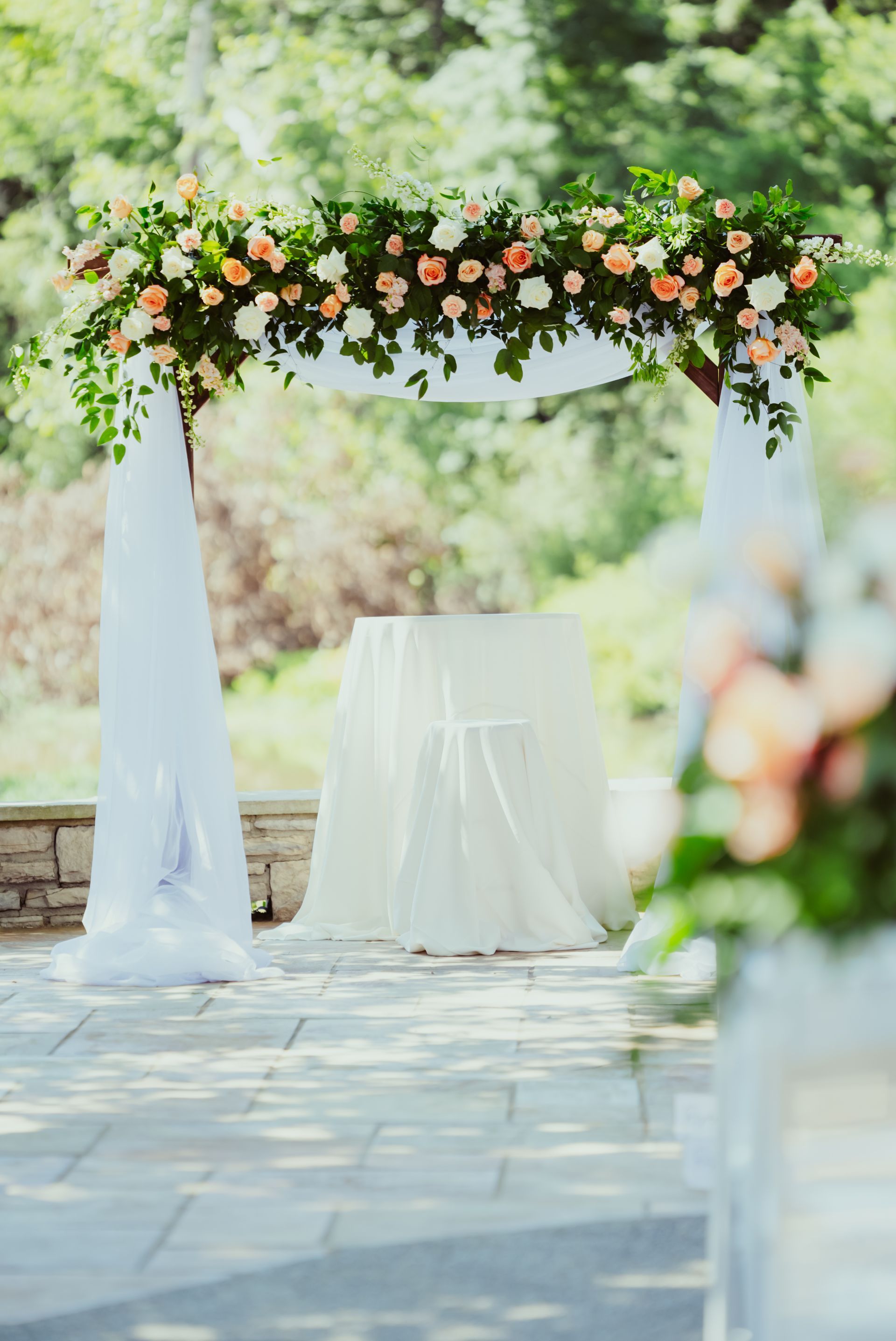 A wedding arch decorated with flowers and leaves is in the middle of a park.