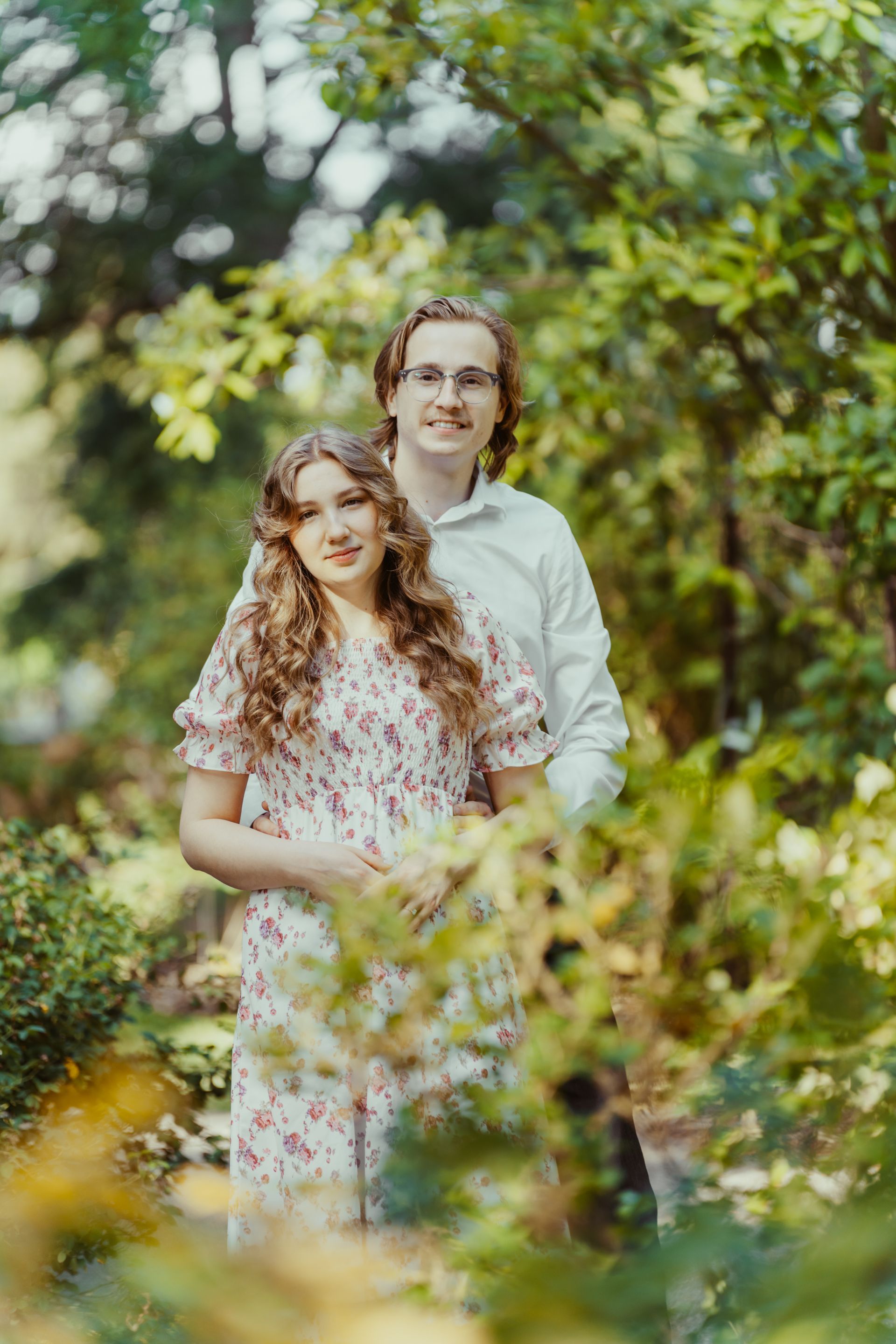 A man and a woman are posing for a picture in the woods.