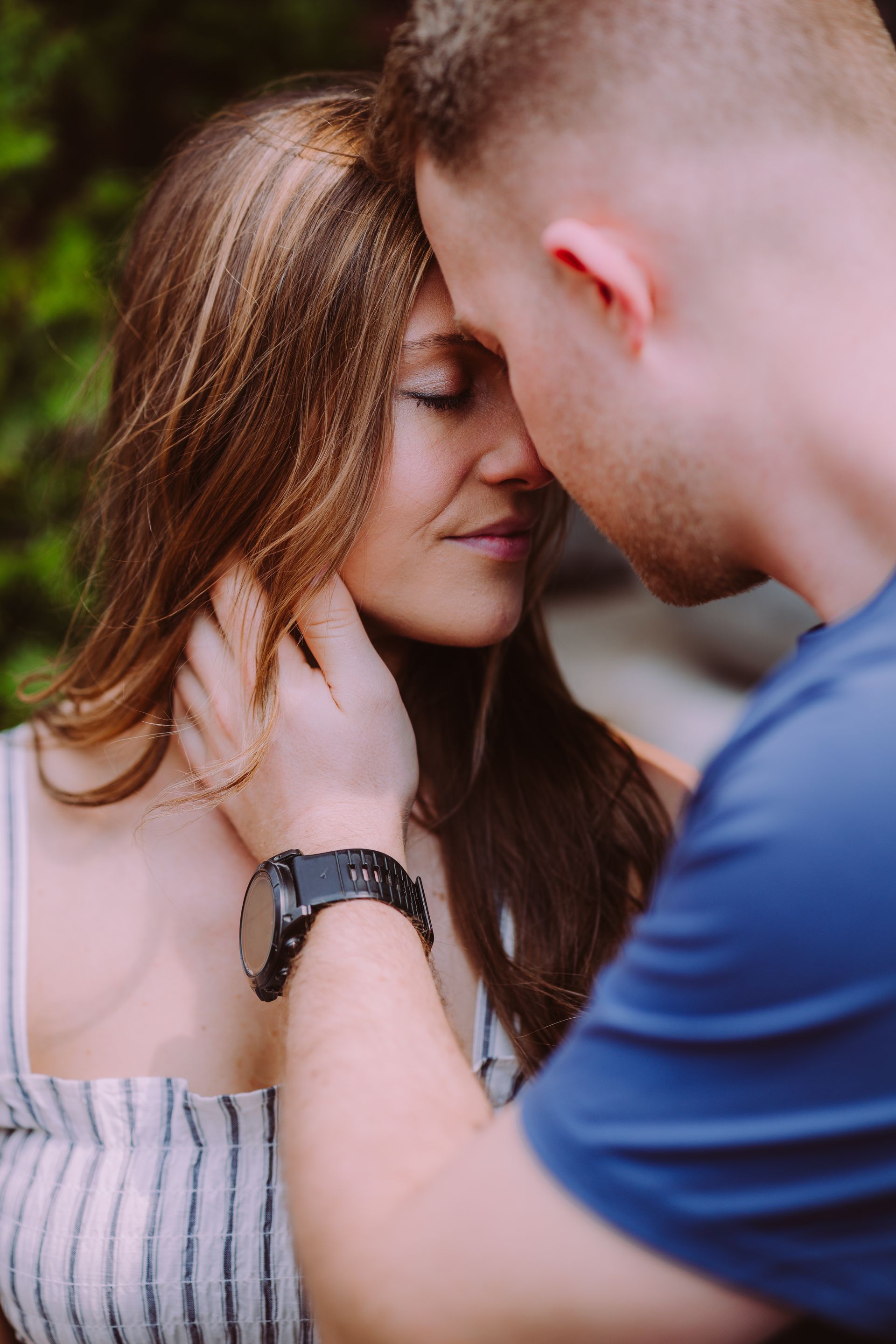 A person gently cups the face of another, who has eyes closed in a moment of intimacy outdoors.