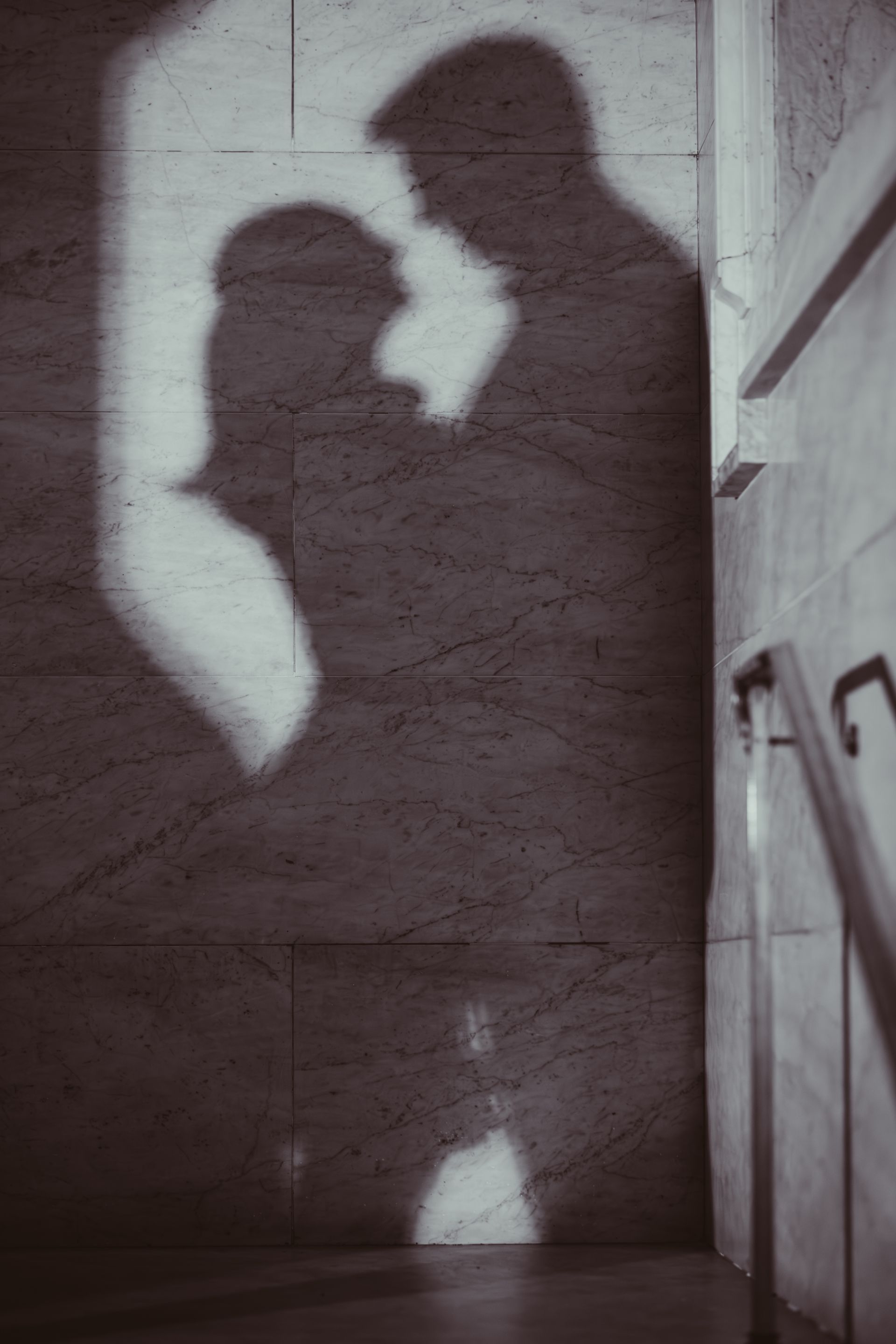 Silhouettes of a couple embracing on a wall in dim light, with stairs at right