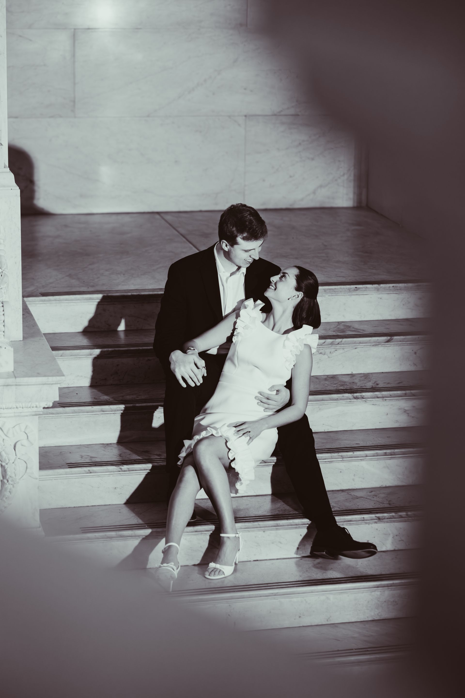 Couple seated on steps, leaning toward each other in dramatic black-and-white lighting