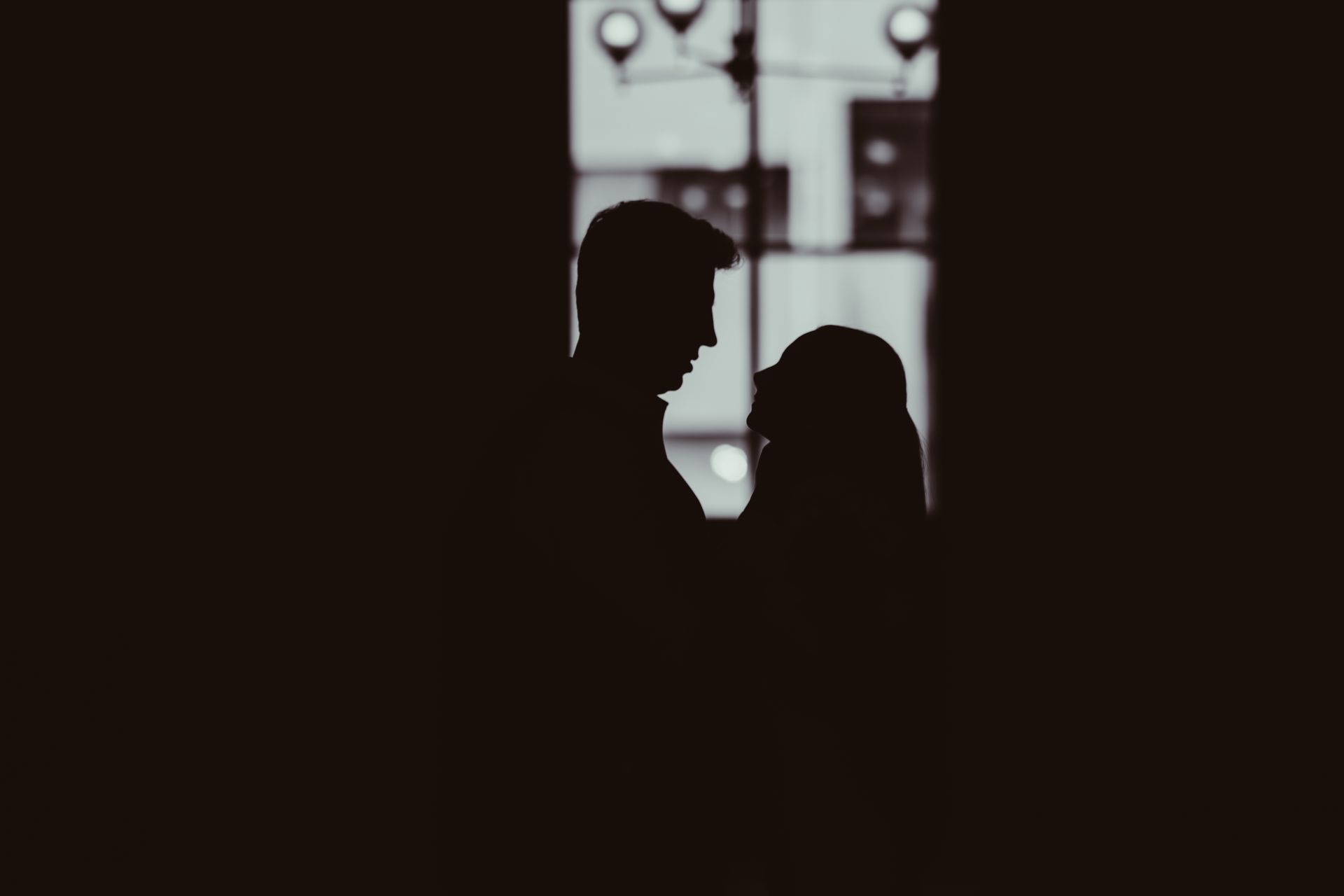 Silhouetted two people facing each other indoors near a bright window