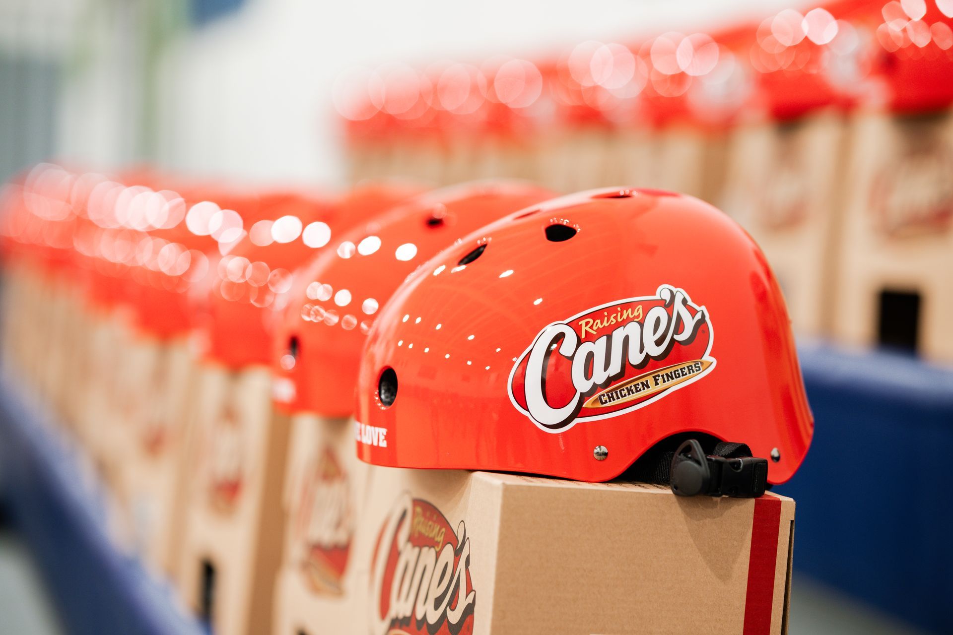A row of bright orange branded Raising Cane's helmets sits atop matching cardboard boxes.