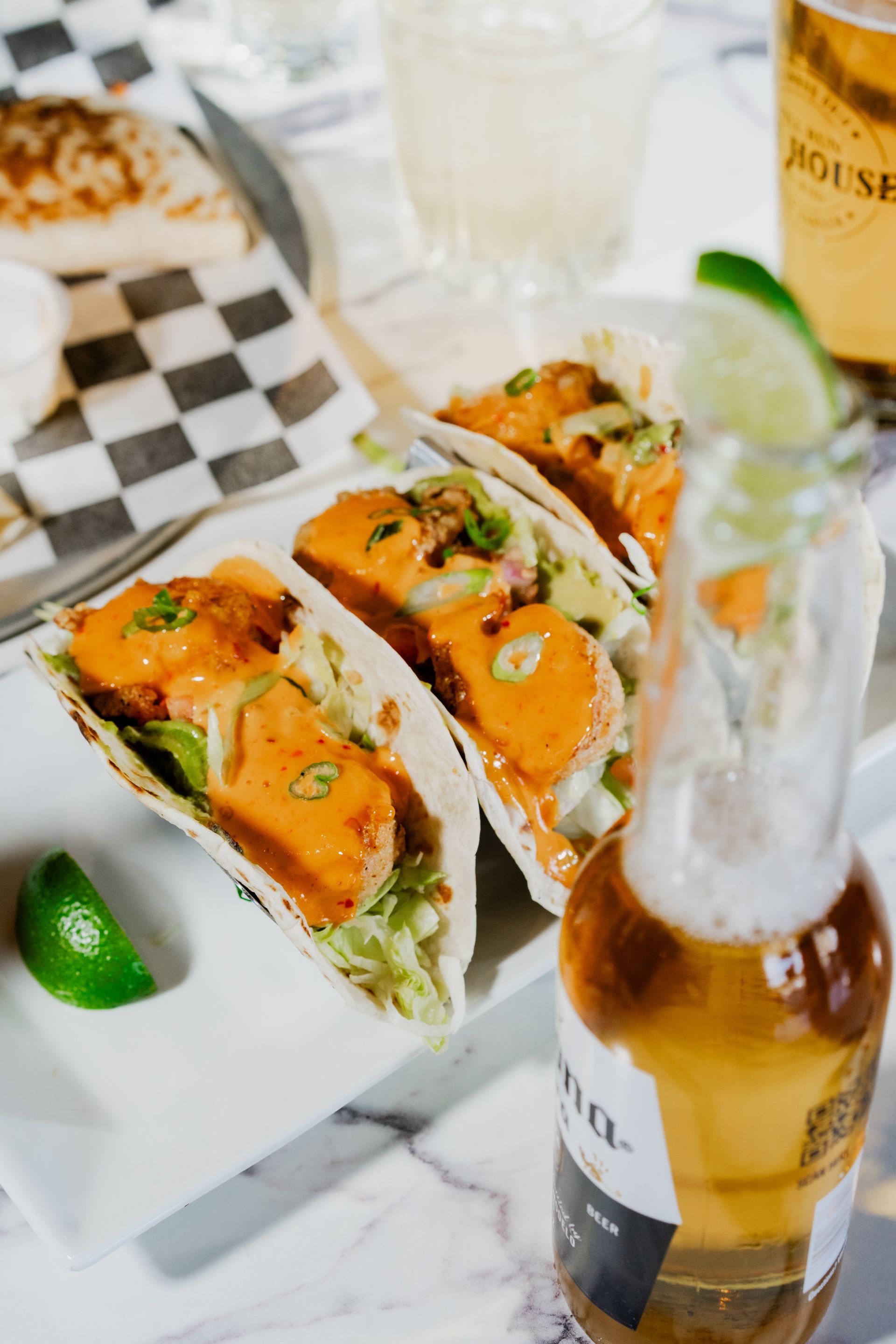 Tacos with orange sauce on a white plate, lime wedge, and beer bottle.