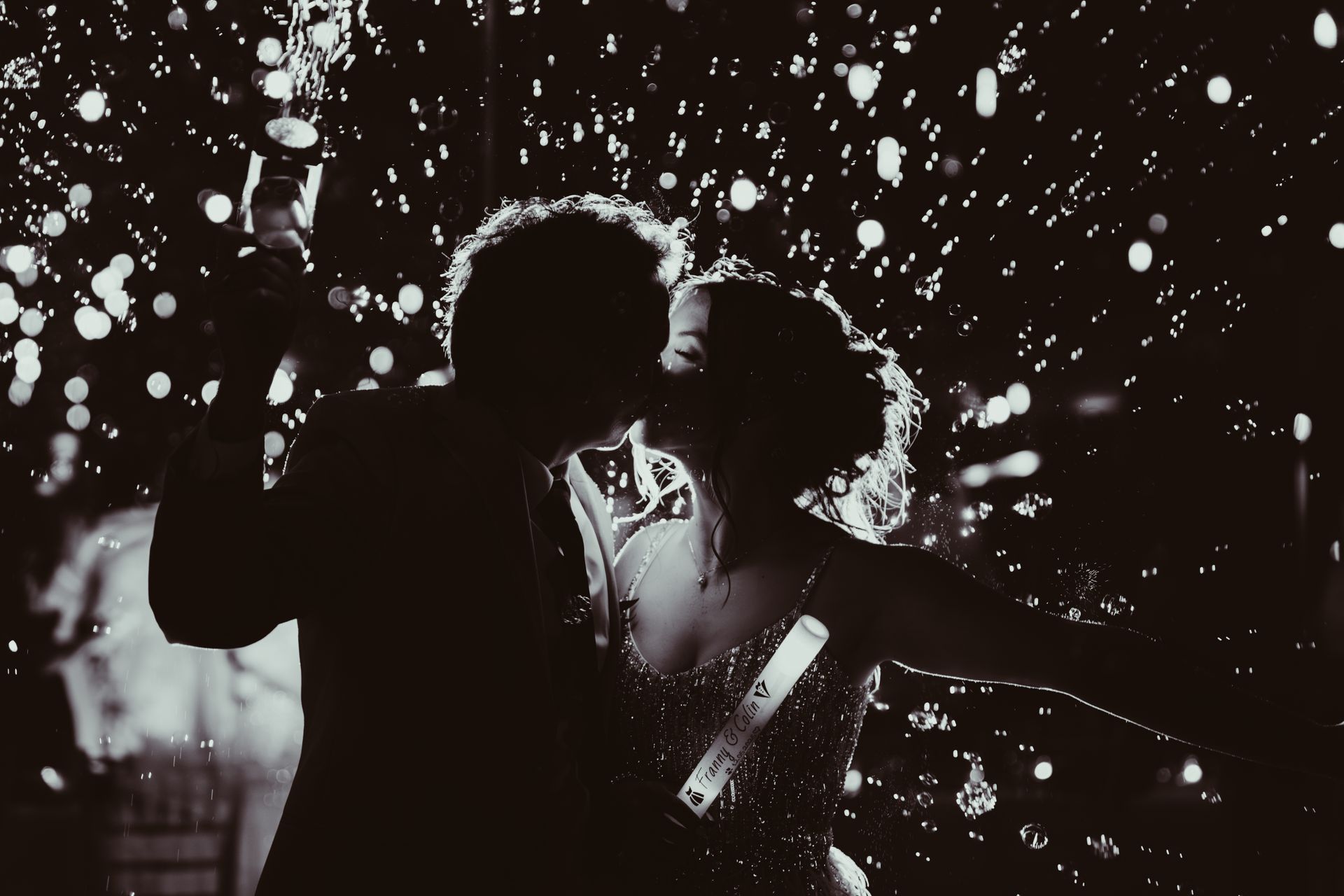 Couple kissing in confetti, silhouetted against a dark background, celebrating.