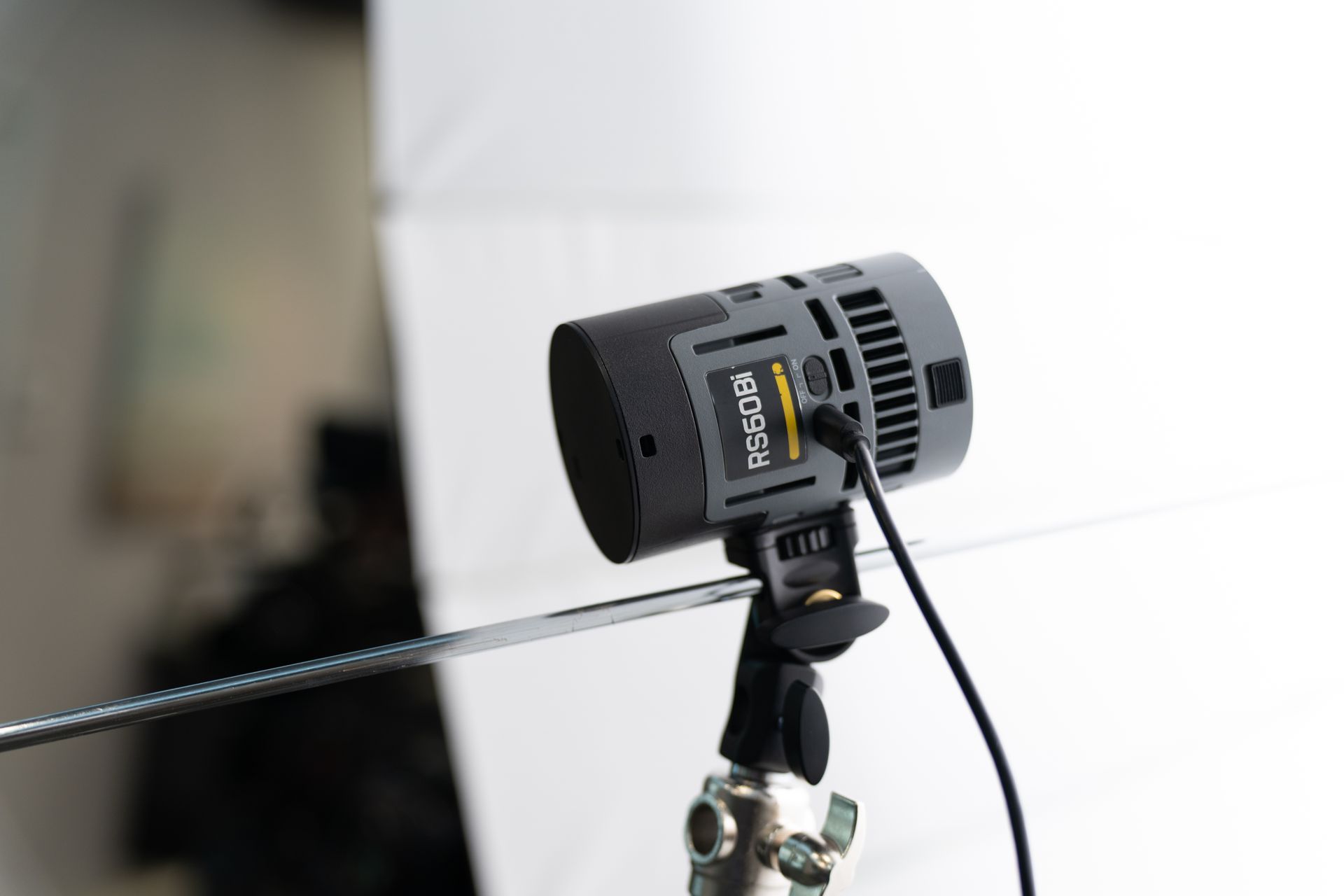 Black studio light, mounted on a stand, angled towards a white softbox in a studio setting.
