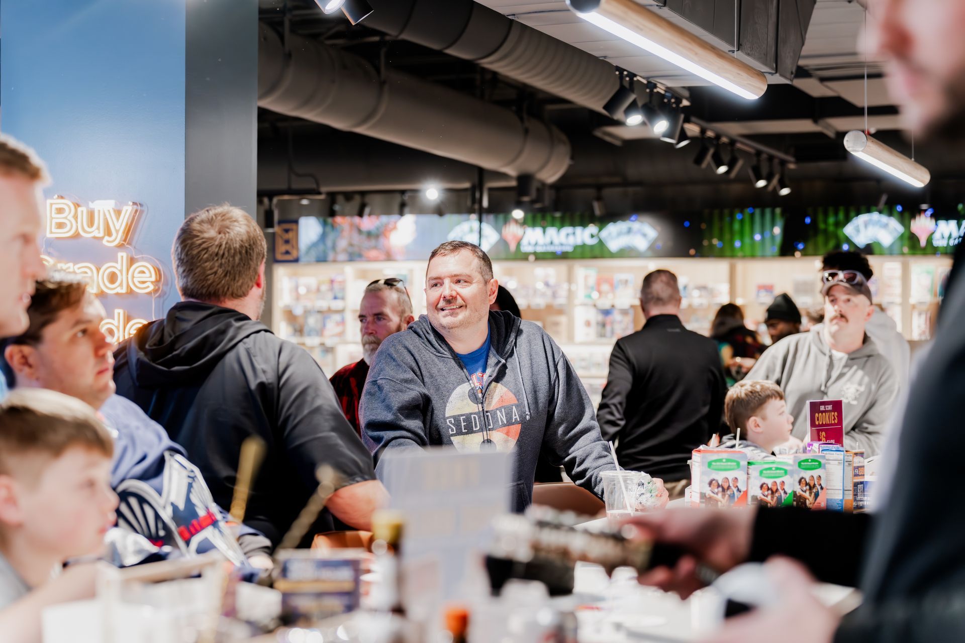 People gather at a game store counter; a man smiles. Store sign reads 